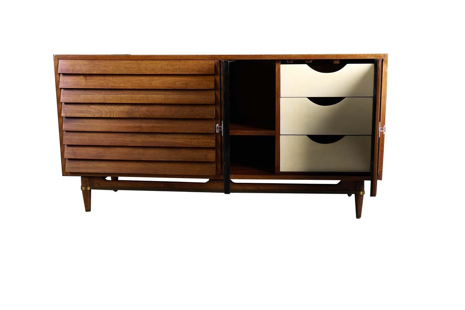 A beautifully detailed proportioned walnut American of Martinsville credenza in great original condition. Designed by Merton Gershun for the “Dania” line featuring rectangular top over a two door mirrored cabinet on the right side, open to reveal