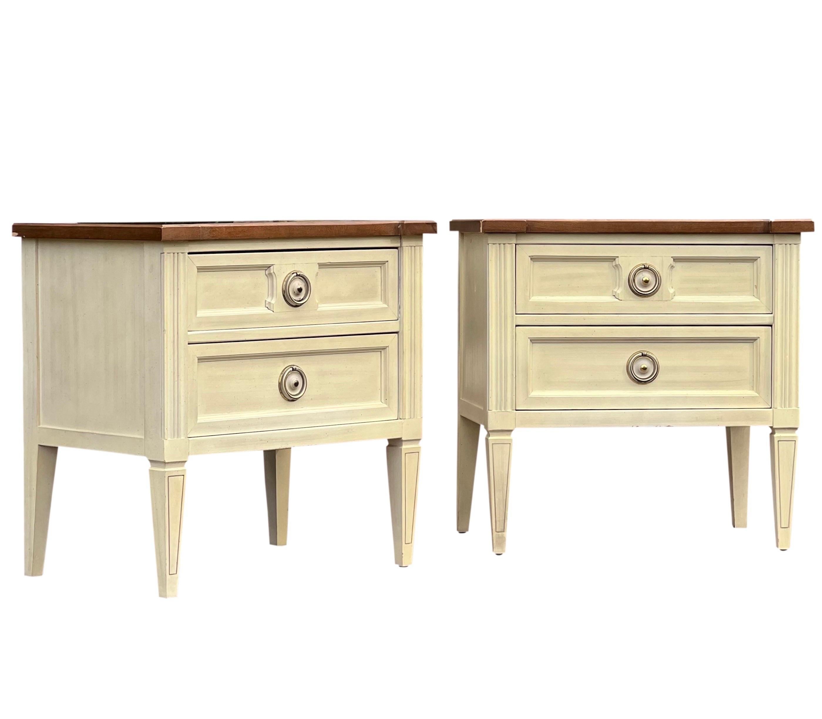 Pair of American of Martinsville Italian style nightstands.

The stands are in original creamy white with a woodgrain parquet top. They feature two drawers with classic brass ring pulls and elegant carved details. Beautiful pair in good condition.