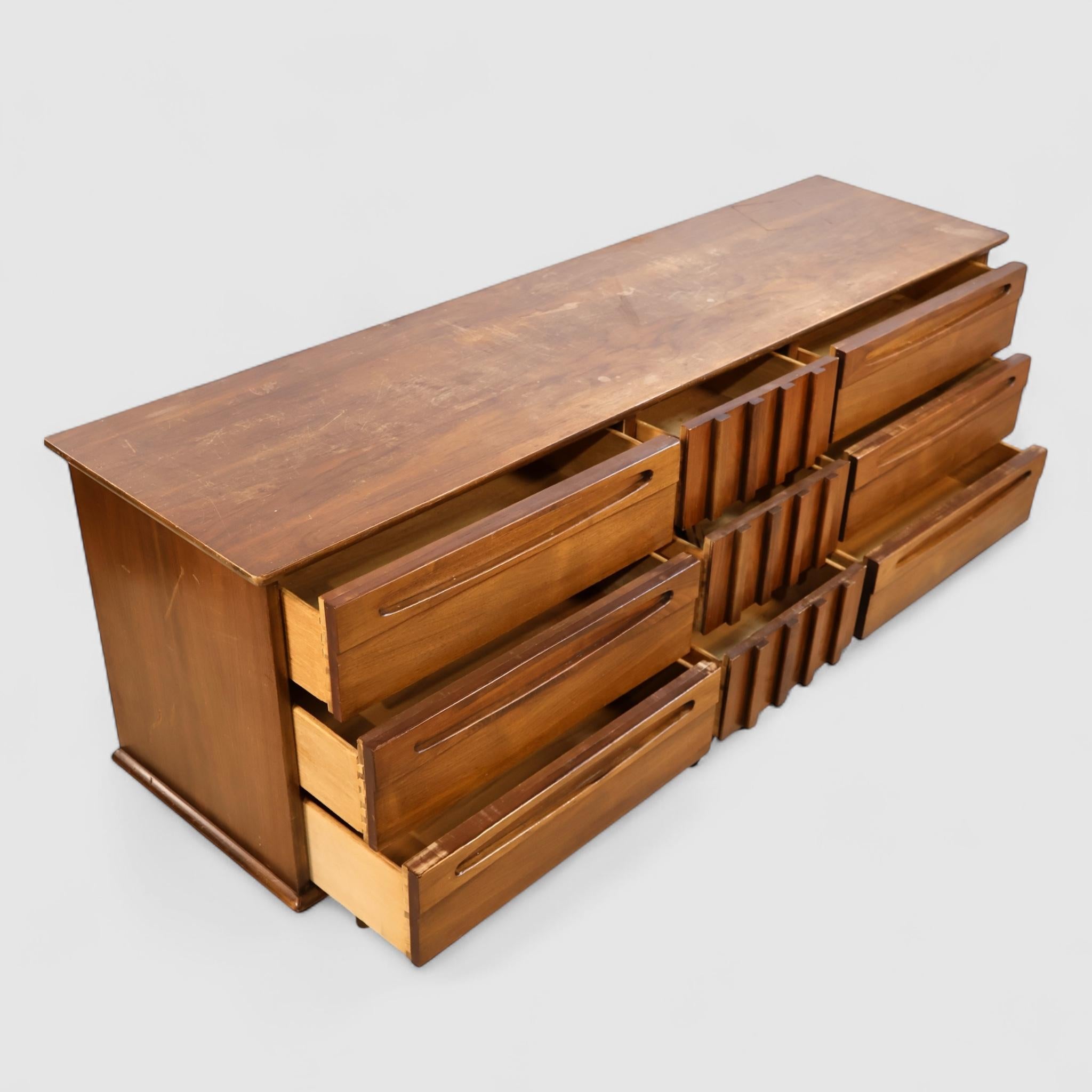 This vintage 1960s lowboy dresser by American of Martinsville blends bold Brutalist influence with refined mid-century craftsmanship. The sculptural front showcases a rhythmic block motif at center, flanked by smooth, sculpted drawer pulls across a