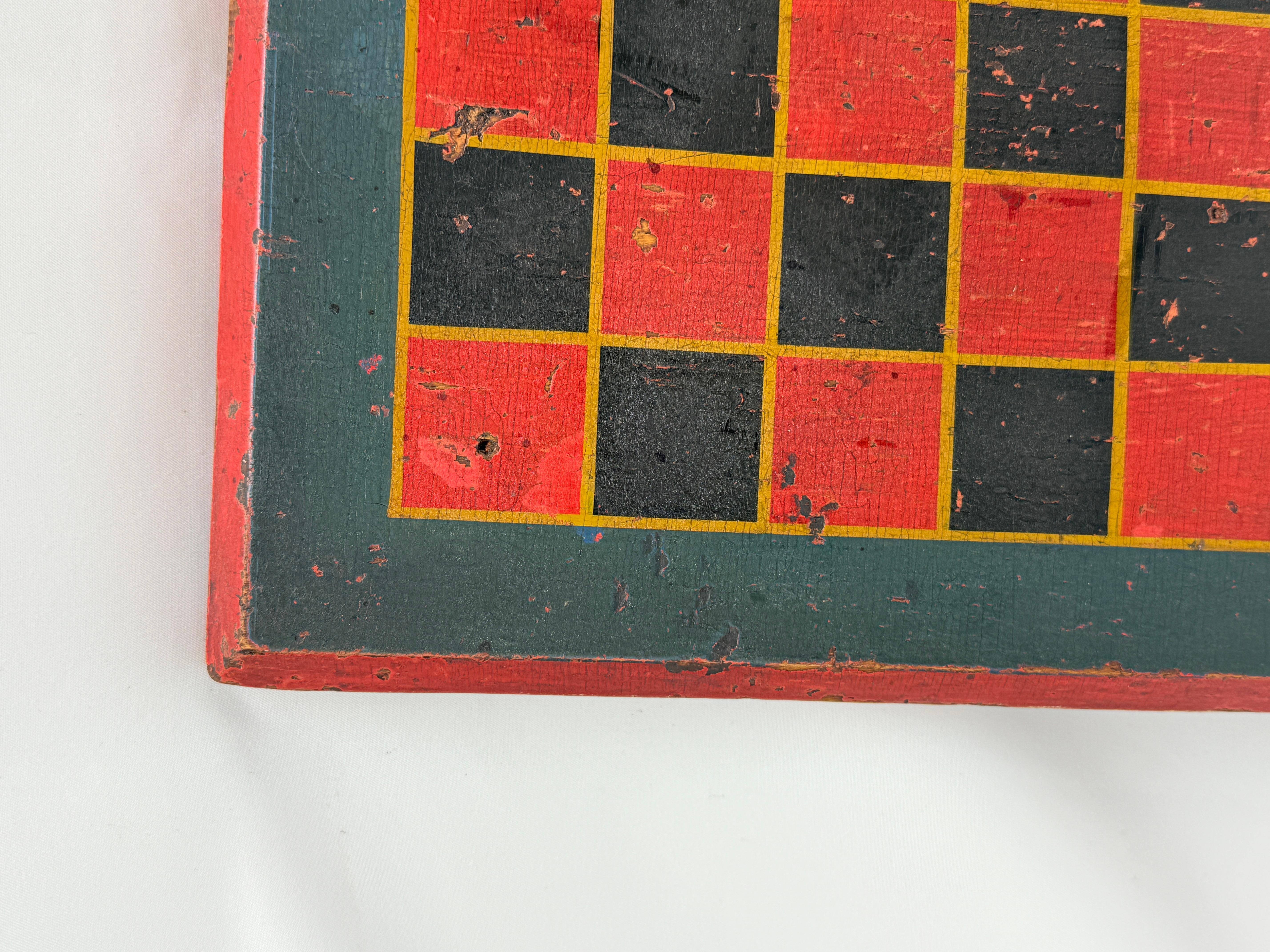 A boldly graphic American folk art game board, hand-painted in red, black, and forest green with yellow dividing lines, dating to the mid-19th century, circa 1840–1860. Constructed from a single wide board or joined panel with chamfered edges, the