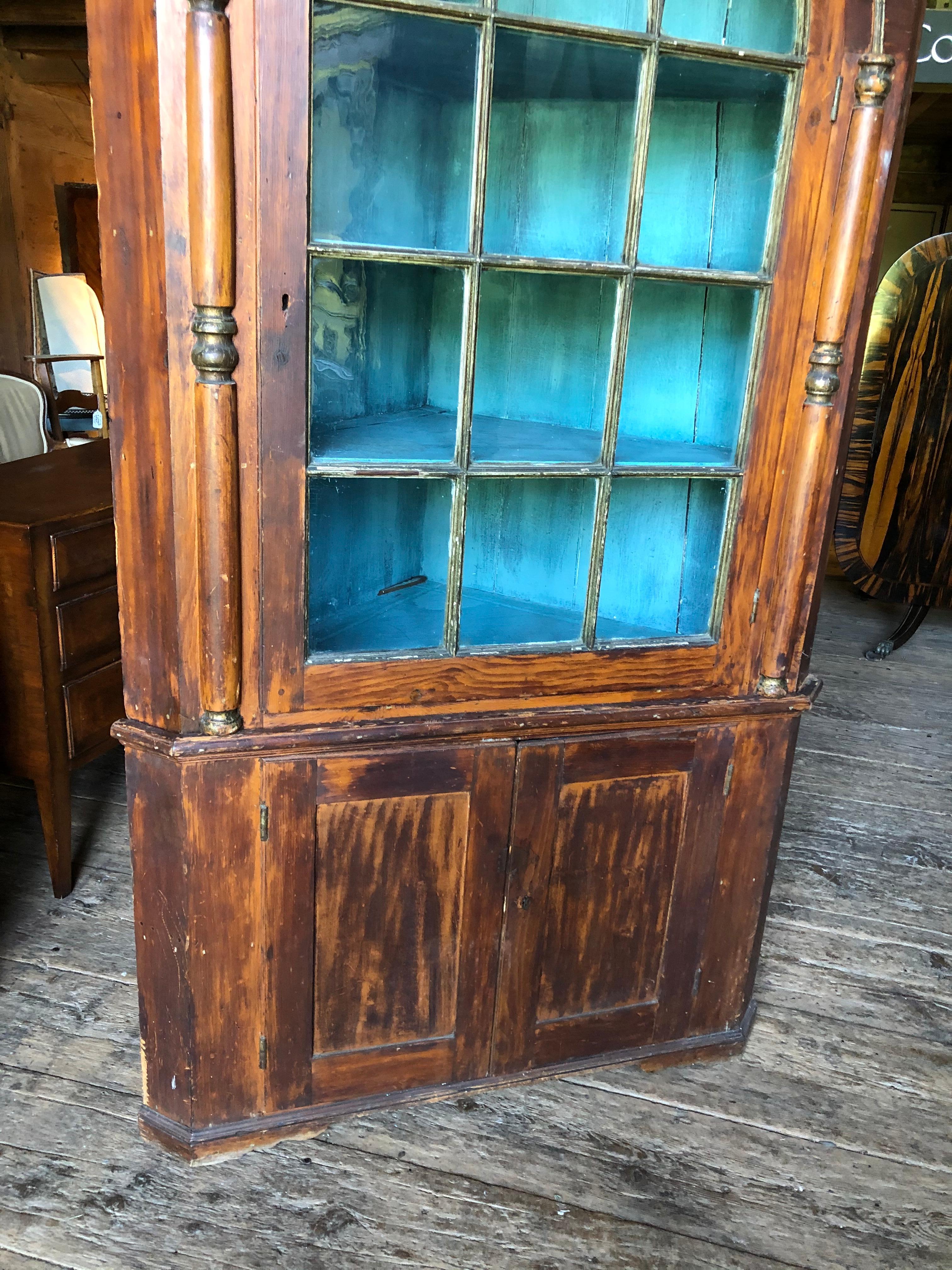 A mid to late 18th century American corner cabinet, the case in faux-painted pine simulating mahogany, probably Pennsylvanian, in 2 parts with upper cabinet having a broken-arch pediment, above a glazed arched door, flanked by applied decorative