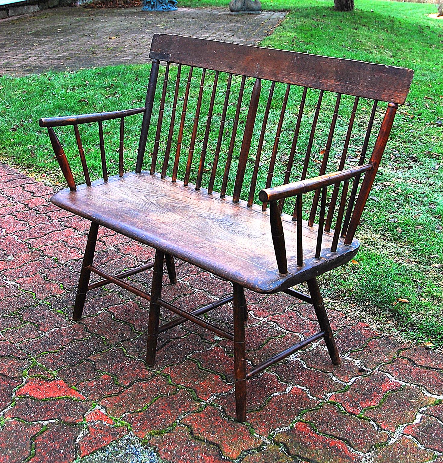 American rare period Windsor settee of the early 19th century, New England origin, bamboo turned ash spindles, stretcher base, single board plank pine seat, six legs, angled top rail. The top rail has an old small patch and there are small shrinkage
