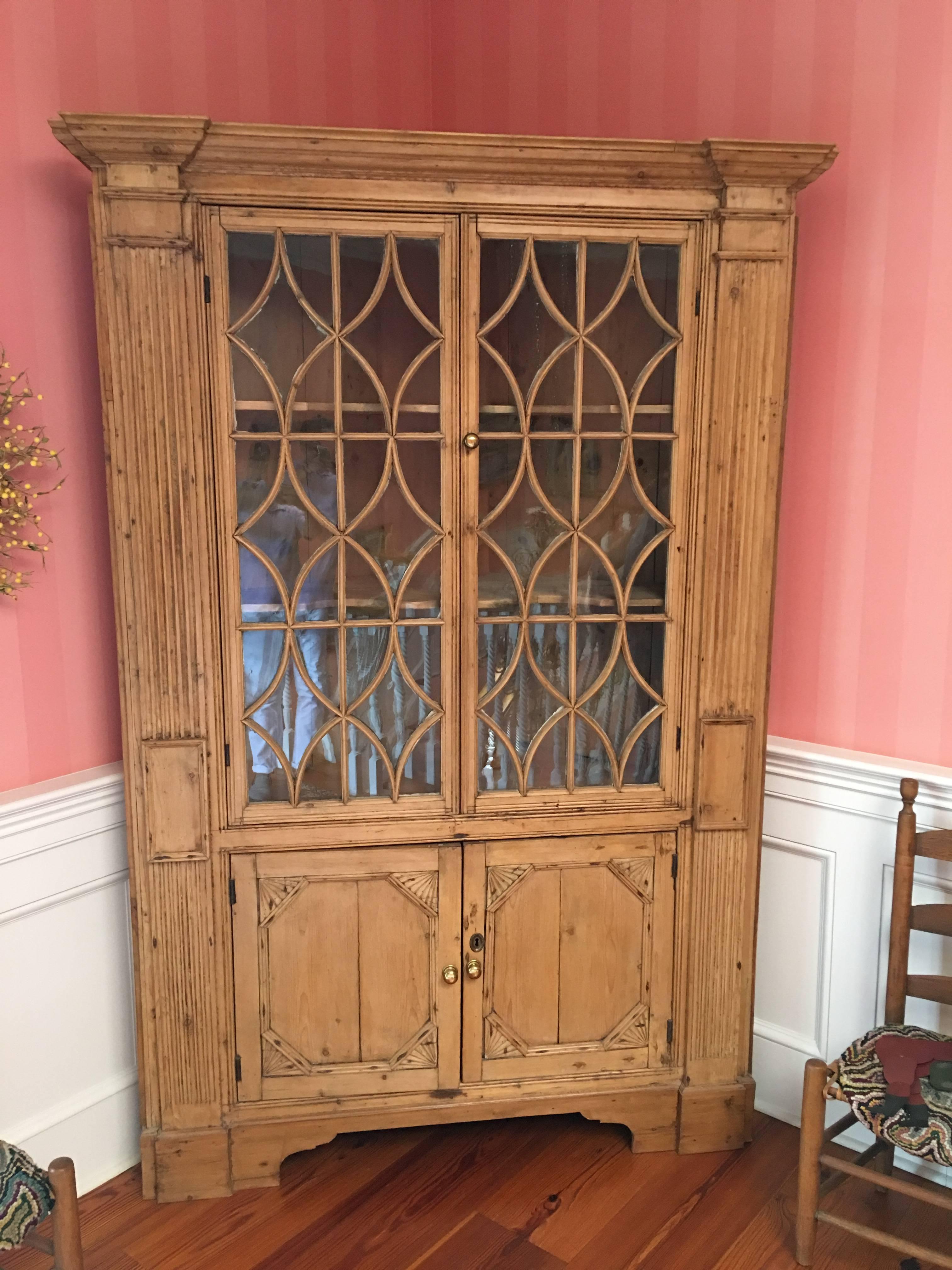 American pine corner cupboard or cabinet with glass doors over two smaller wood doors, 19th century. It features a complex molded break-fronted cornice, surmounting a substantial case flanked by reeded pilasters bracketing two glazed doors, fitted