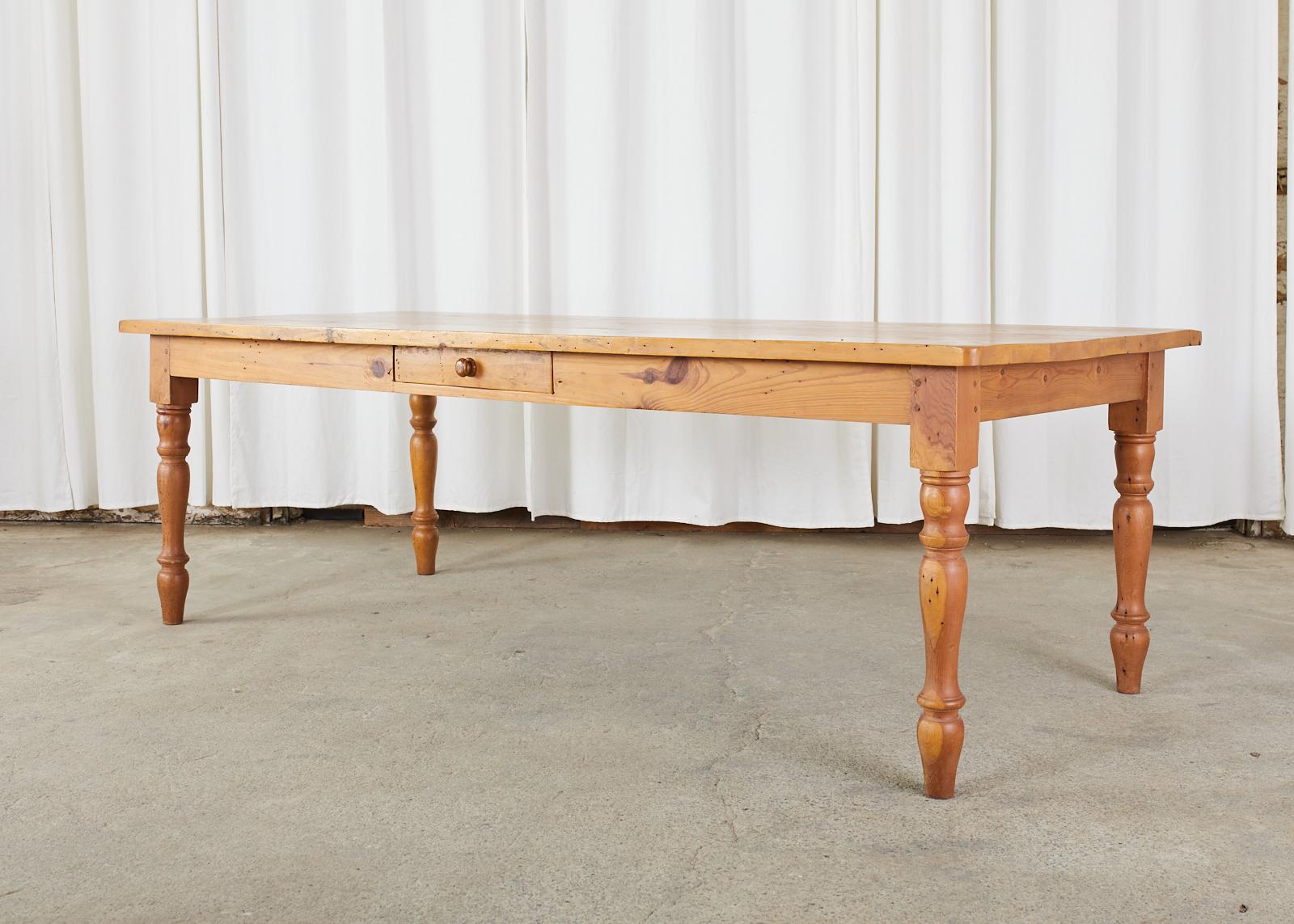 Rustic American pine dining table made in the country farmhouse style. The large top is made from 1.25 inch thick planks of pine. Supported by thick, turned legs on each corner. Ample legroom measuring 25 inches from the floor to the apron. The