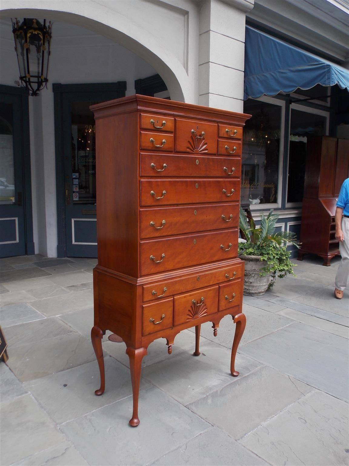 American Queen Anne cherry flat top highboy with a molded edge cornice, two flanking upper case drawers with a centered fan carved drawer and four lower graduated drawers retaining the original brasses. Lower case has a carved molded edge with a