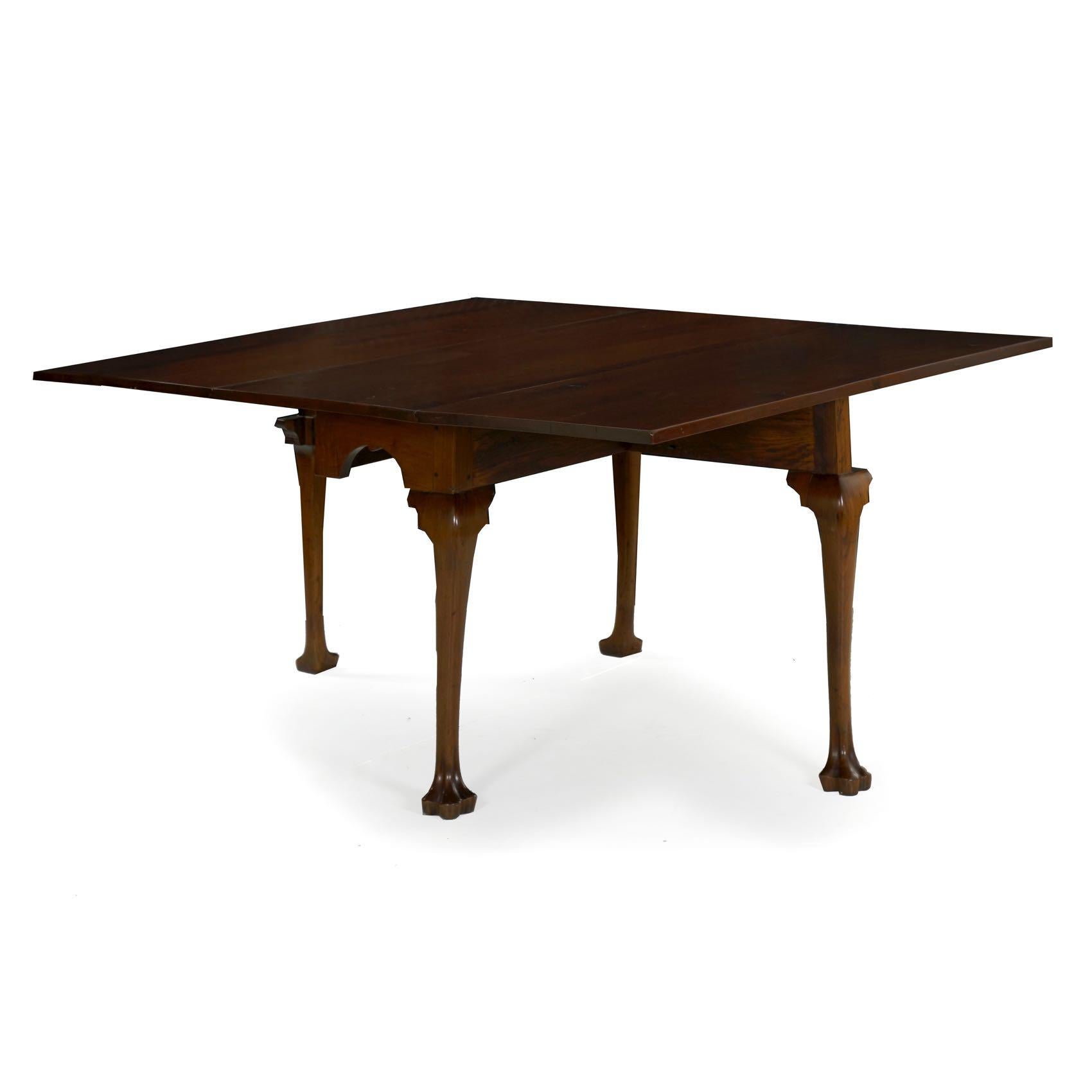 A fine Queen Anne walnut drop-leaf dining table from the third quarter of the 18th century, it is characterized by an arched skirt with a tiny drop at the centre over cabriole legs terminating in carved trifid feet. The leaves are raised over