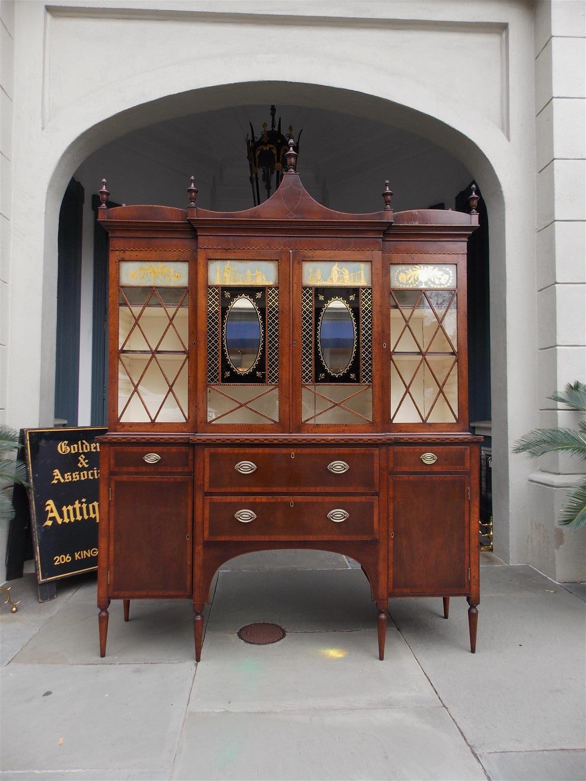 American Regency mahogany breakfront bookcase with a carved serpentine cornice, turned urn flame finials, checkered inlays, upper case with four hinged doors consisting of figural and floral hand painted gilt églomisé glass panels, adjustable