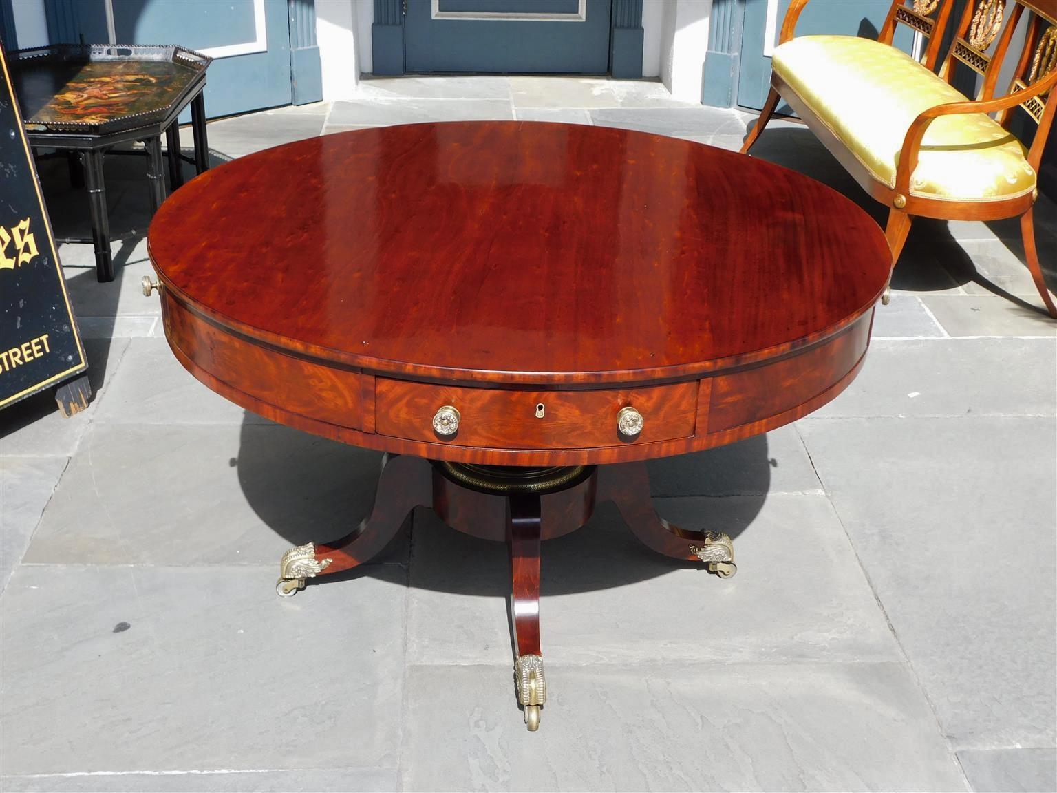 American Regency mahogany four drawer circular center table with a fitted interior writing desk, foliage brass pulls, key hole escutcheons, central support column with decorative brass ring, and resting on saber legs with the original floral brass
