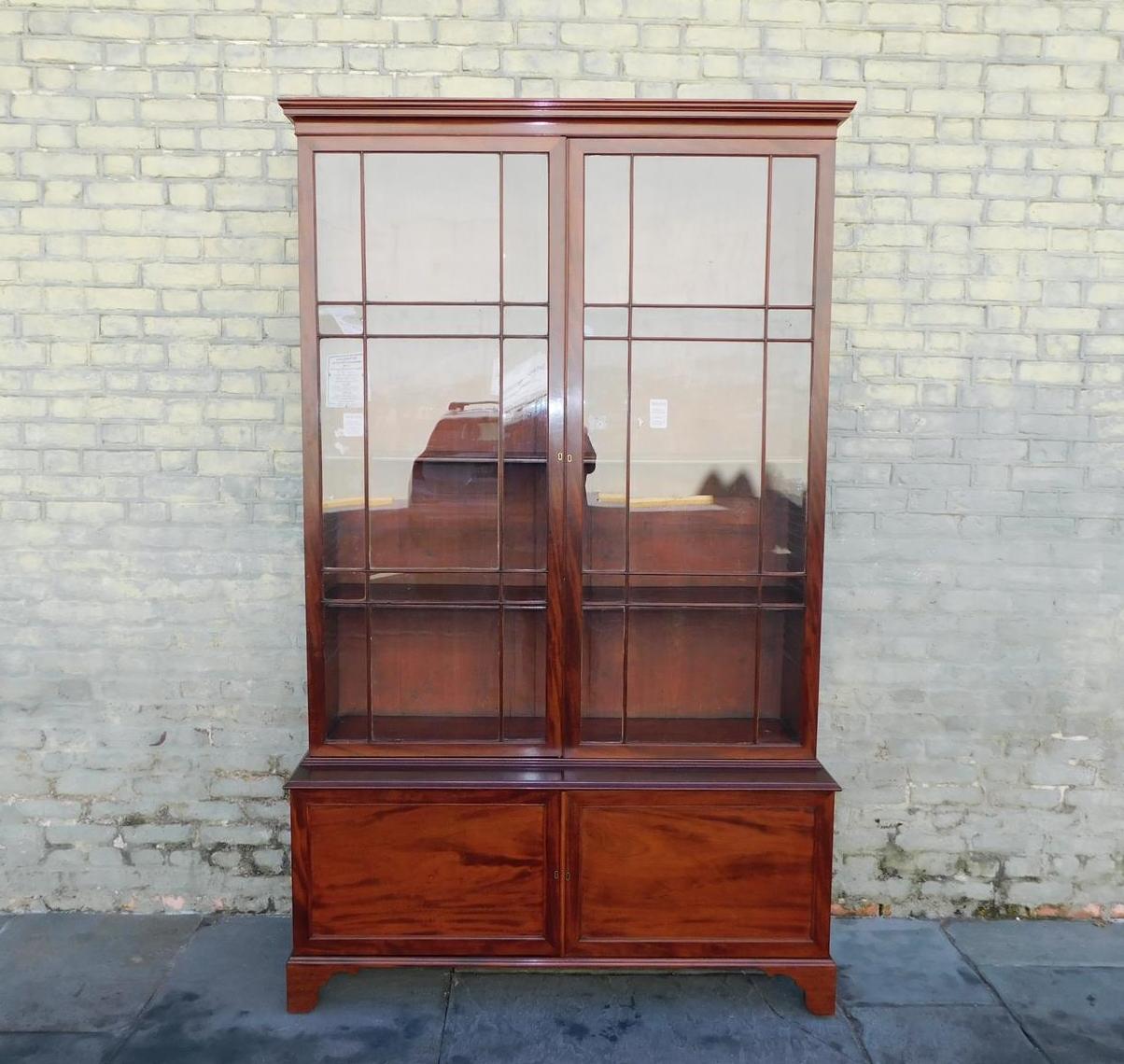 Bibliothèque en acajou de style Régence américaine avec une corniche moulurée et sculptée, des portes à charnières sur le côté supérieur avec verre d'origine révélant trois étagères intérieures réglables, des serrures d'origine avec clé, des portes