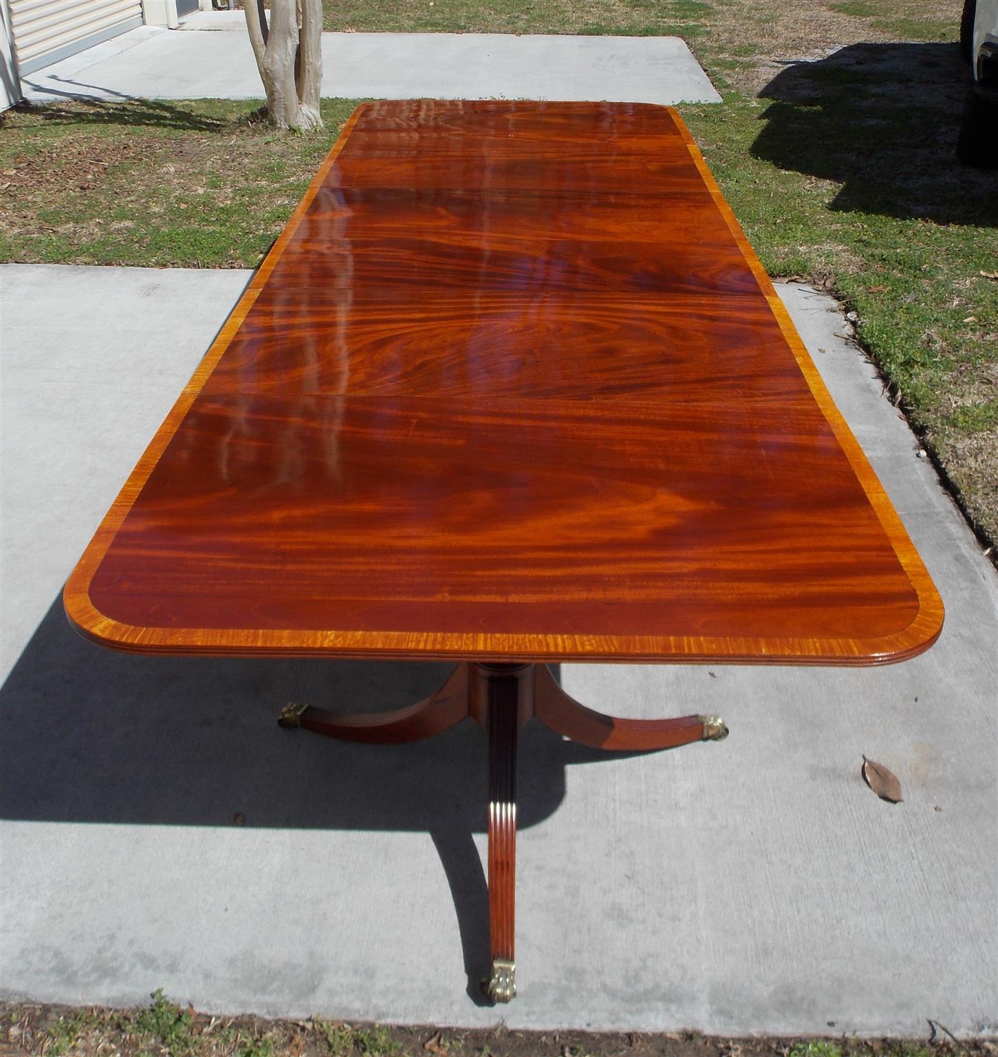 American Regency Honduran mahogany triple pedestal dining room table with satinwood edge banding, bulbous ringed pedestals, and resting on splayed reeded legs with the original brass lions paw casters, Early 19th century.
Table has two removable 23