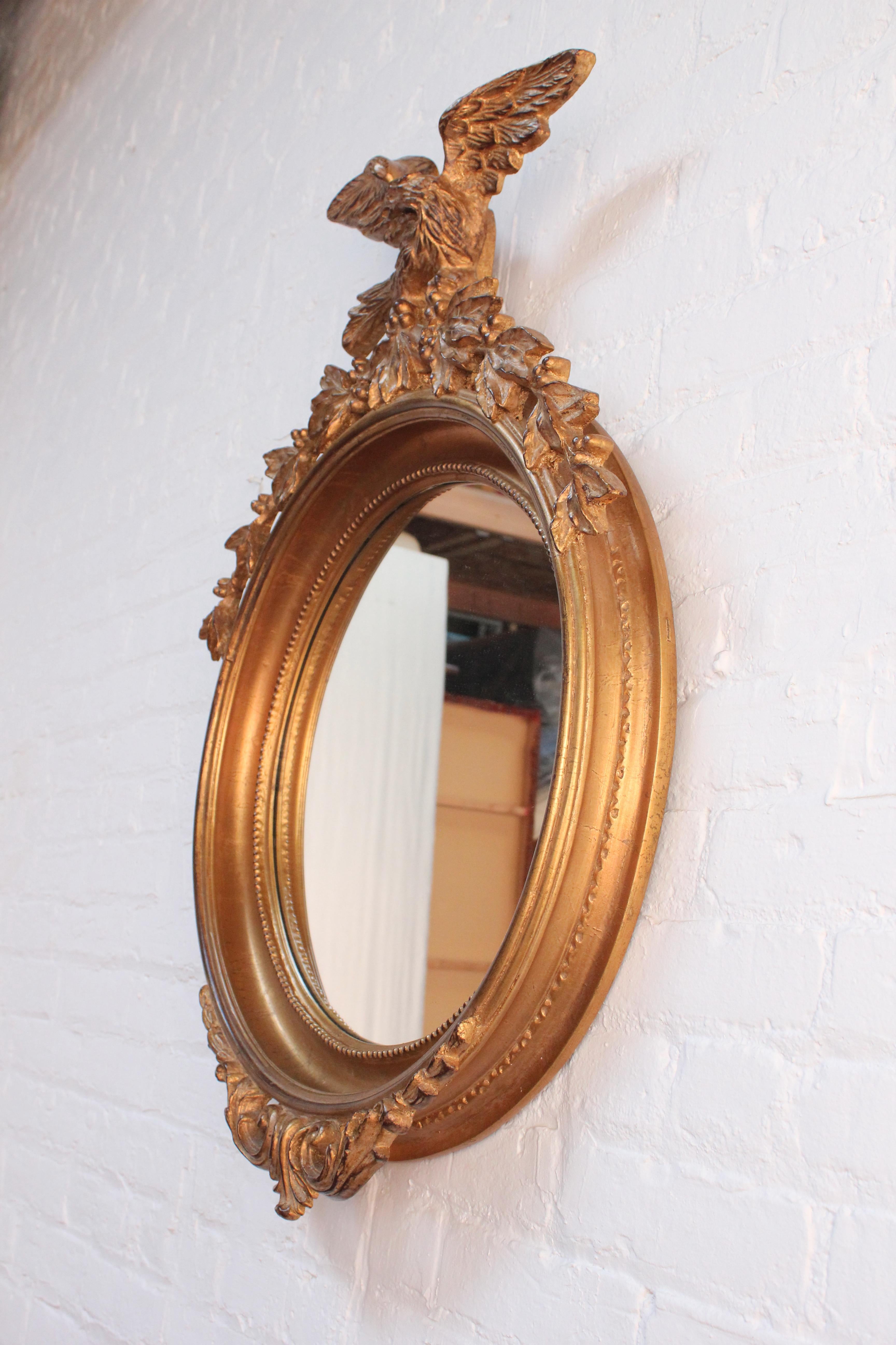 Substantial Federal-Style mirror featuring inset glass (not convex) within a deep, gilt resin frame adorned by an eagle perched on laurel at the top and acanthus detail below (ca. Mid 20th Century, USA). 
Gilt / leaf shows good age / natural patina