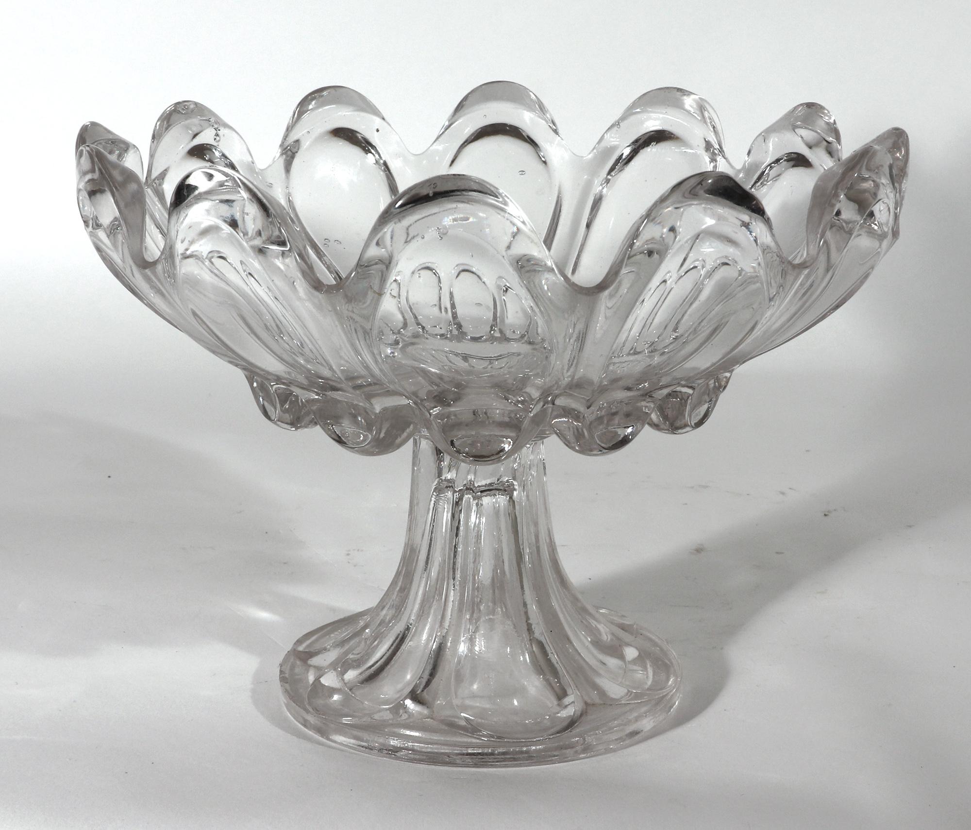 American sandwich glass lobed compote
Mid-19th century

The circular glass footed compote with twelve lobes forming an undulating rim. The upper bowl raised on a hollow flaring foot.

Dimensions: 7 inches high x 9 1/4 inch diameter

