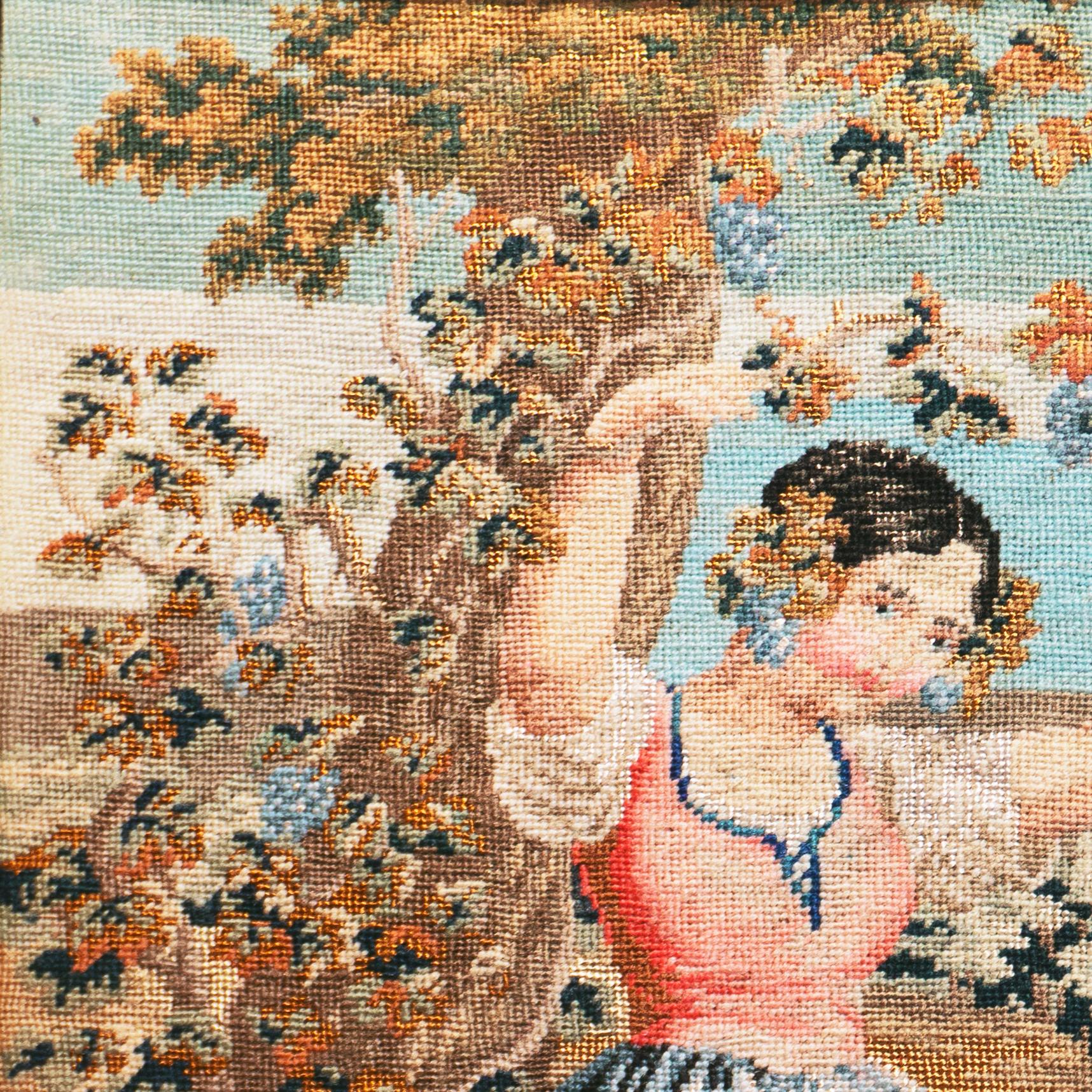 An unusually fine and delicate, mid-19th American figural needlepoint showing an idyllic view of frontier life with a young girl reaching up on tiptoes towards a grape-laden vine on a tree bough that her mother is lowering within her reach. A