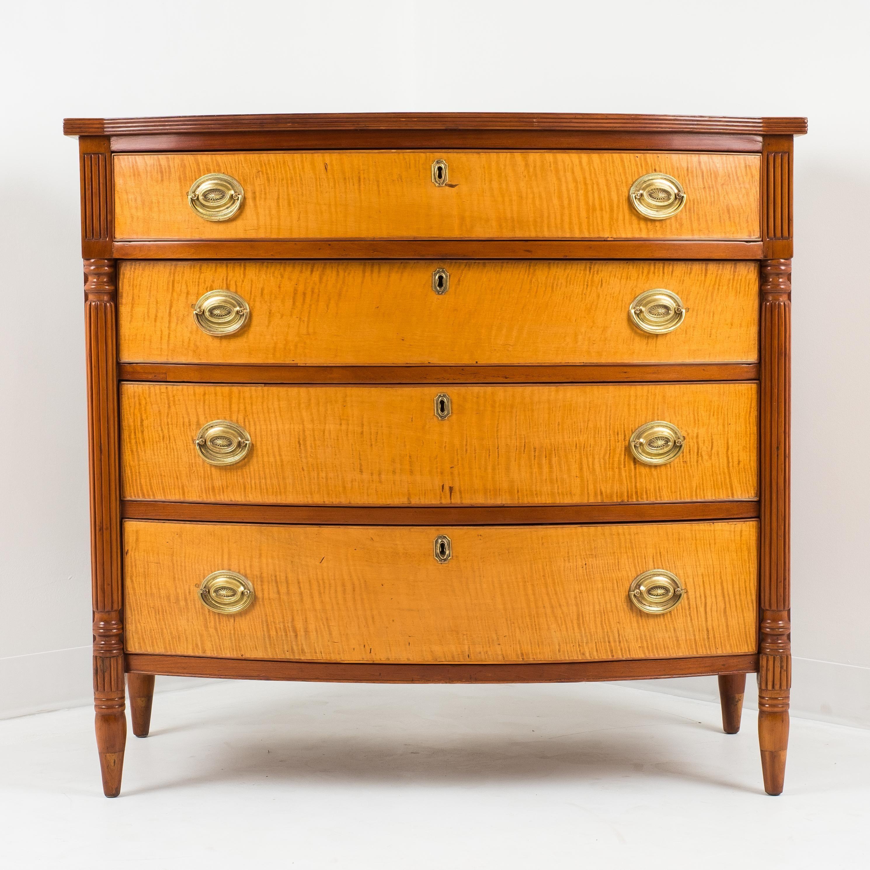American Sheraton four drawer bow front chest with curly maple front and American cherry case. The graduated drawers, with projecting top drawer, are flanked by reeded pilasters which resolve into turned legs. Northern white pine secondary