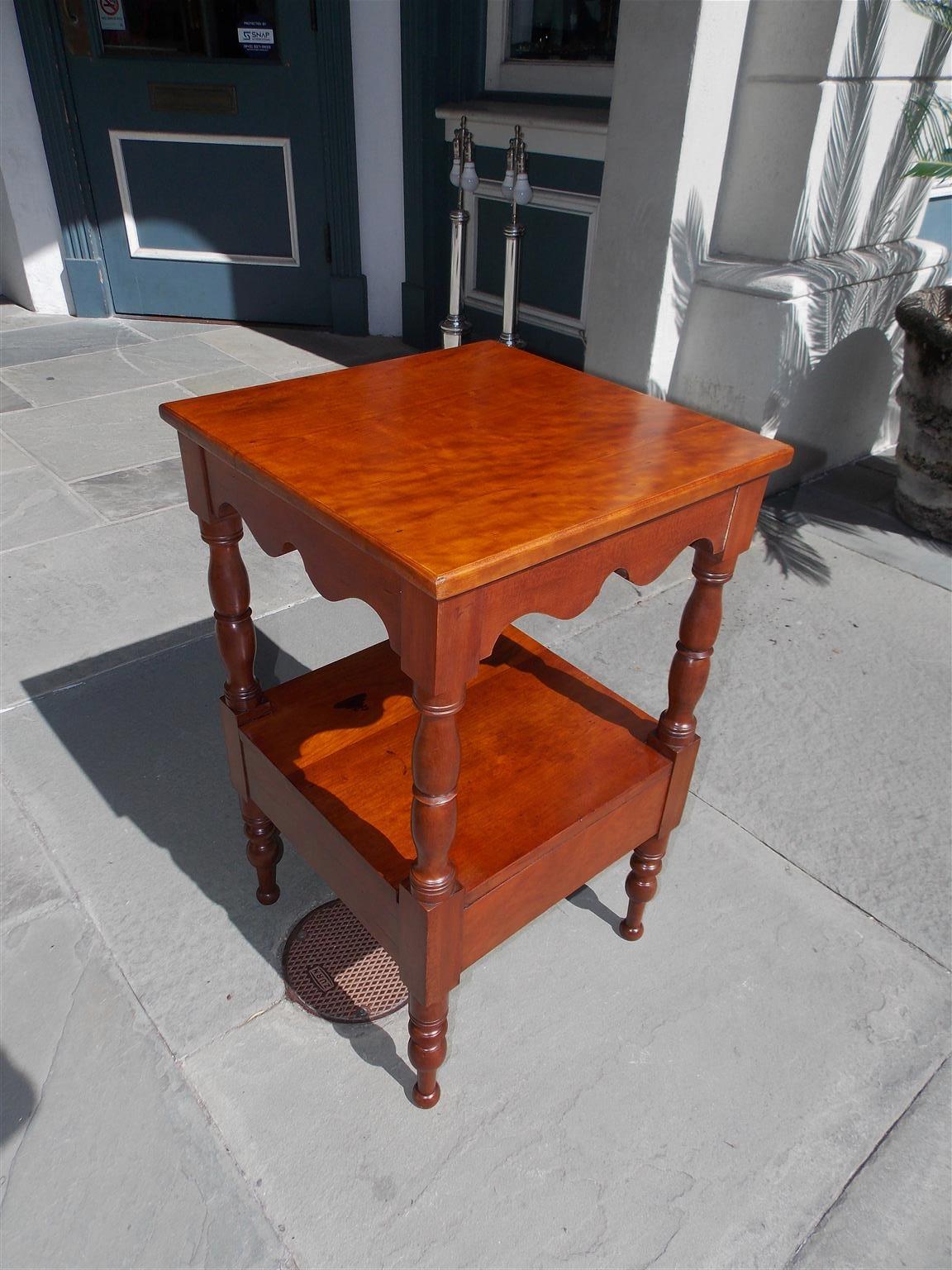 American Sheraton cherry two tiered stand with a straight edge top, scalloped skirt, lower shelf, and resting on the original turned bulbous ringed legs, Early 19th century.