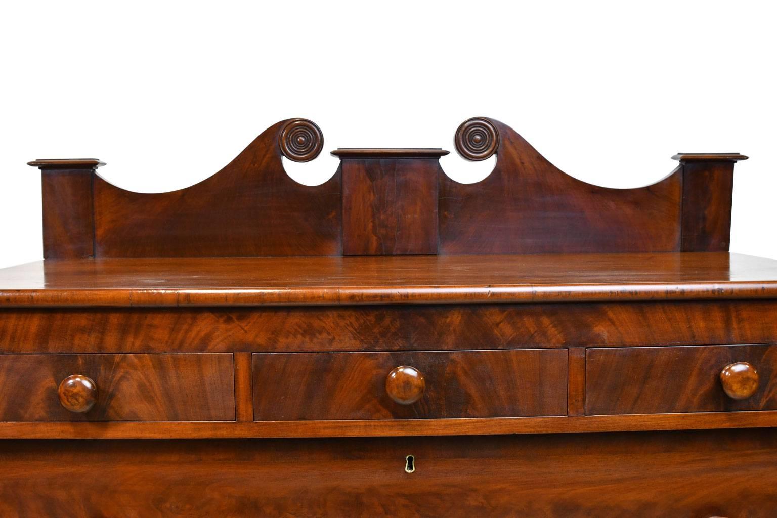 A lovely Sheraton chest in mahogany with three small drawers over four drawers of varying depths cross banded with mahogany. Chest has original turned wooden knobs, backsplash with scrolled split-pediment top, and turned feet, American, circa
