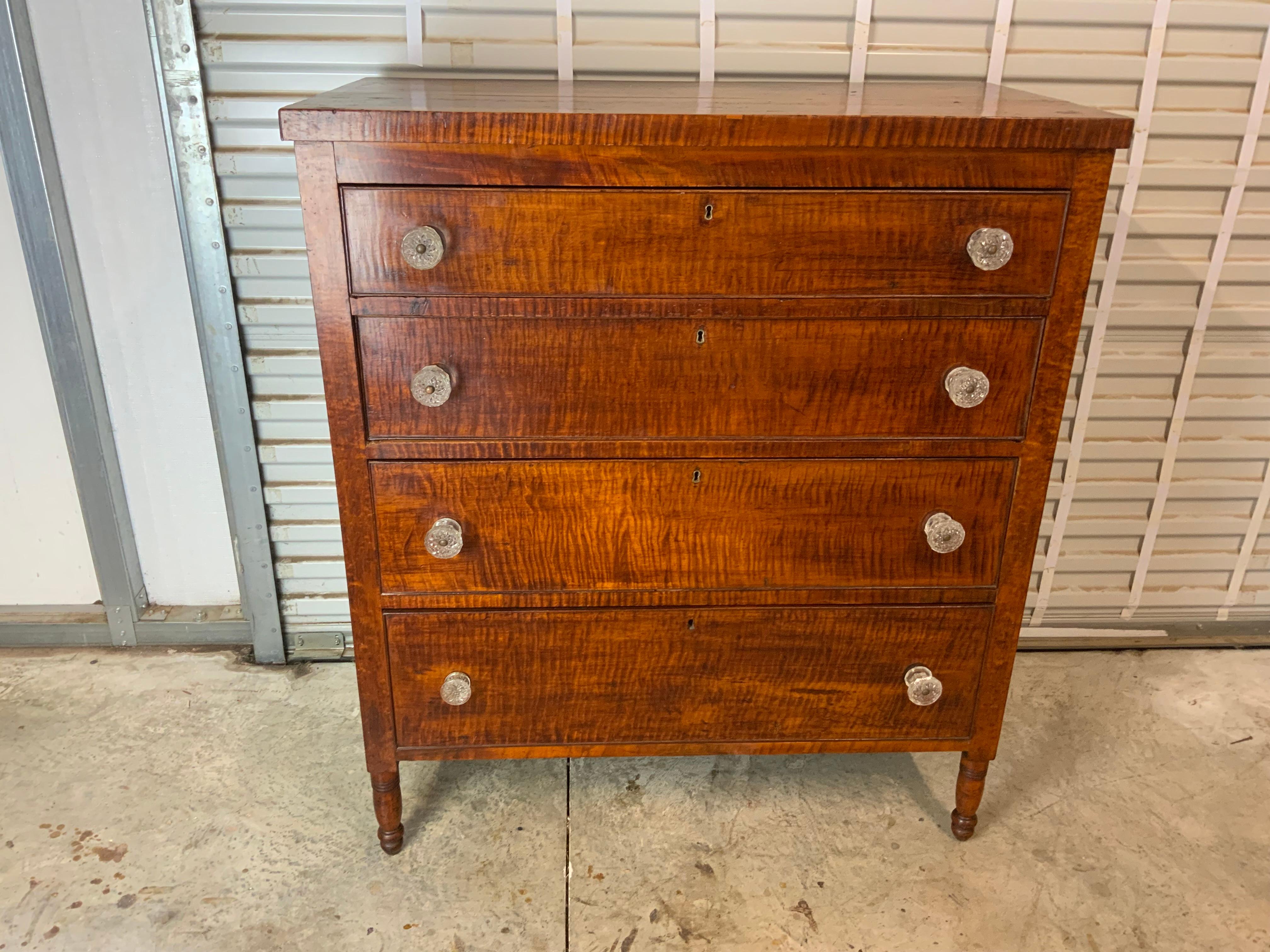 A nicely figured New England Curly Maple Sheraton chest 1815-20. White Pine secondary wood with period glass knobs on the four cock beaded graduated size drawers. Very old and possibly an original surface with a great color and patina. The drawers