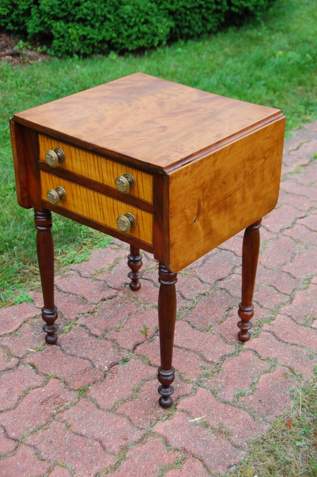 American Sheraton early 19th century dropleaf two drawer side or end table. This sophisticated country table has a mahogany carcass and legs, the top is maple, one leaf of which has a little birdseye maple in evidence; the drawer fronts are curly