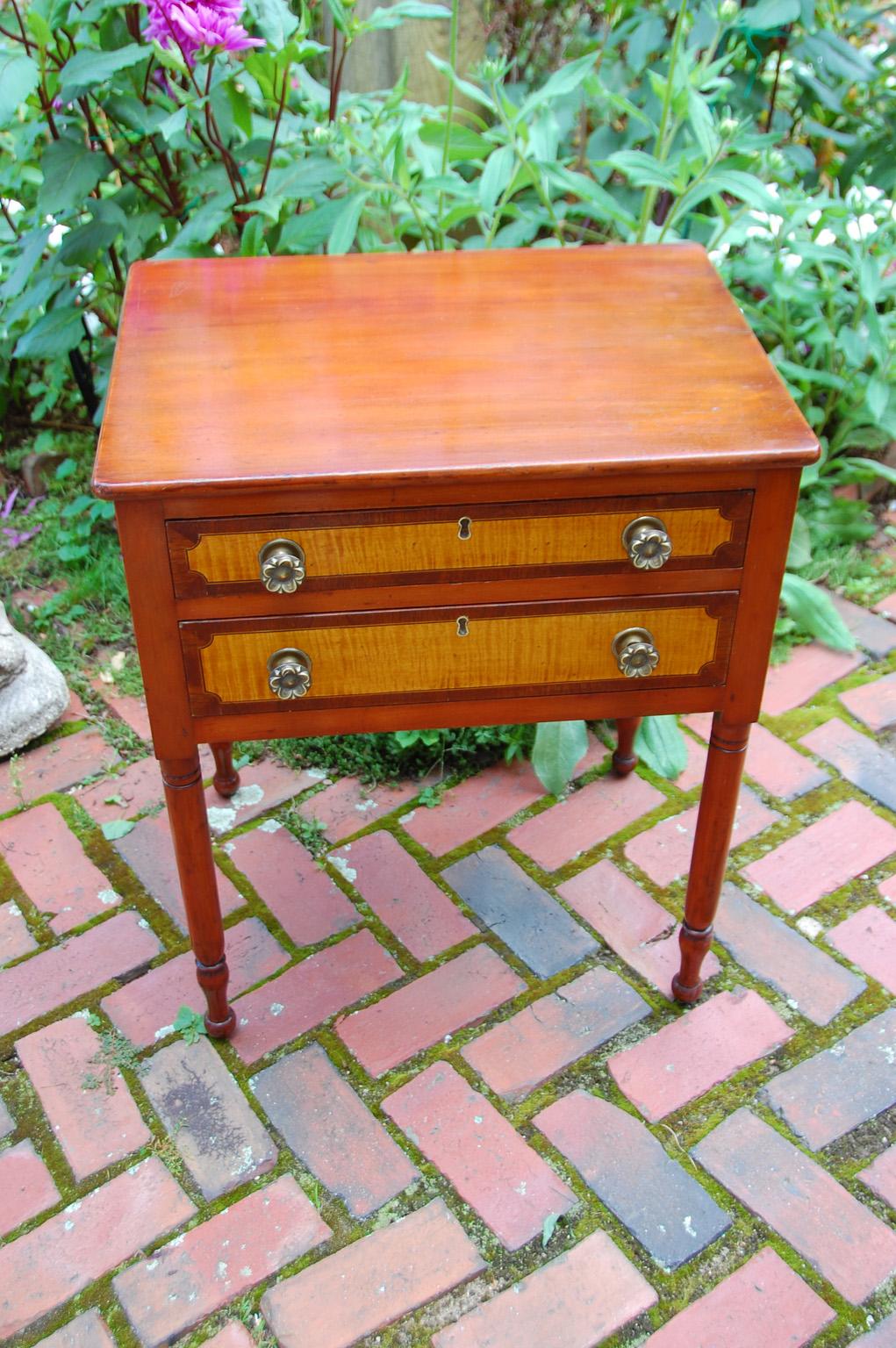 American early 19th century sheraton two drawer maple stand with curly maple drawer fronts enhanced with rosewood crossbanding. The tapered turned legs are in lovely scale to the table which is finished on all sides so it can easily freestand within