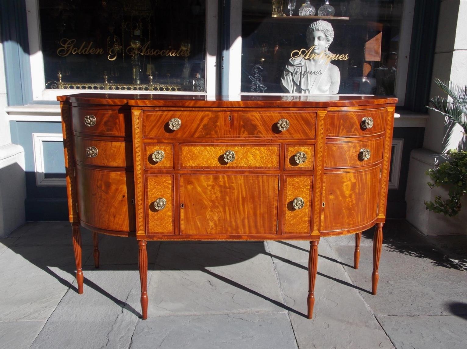 American Sheraton mahogany bow front sideboard with flanking spiral satin wood inlaid capitals, centered drawers with satinwood string inlays, lower bird's-eye maple candle and wine bottle drawers, hinged cabinet doors with interior storage,