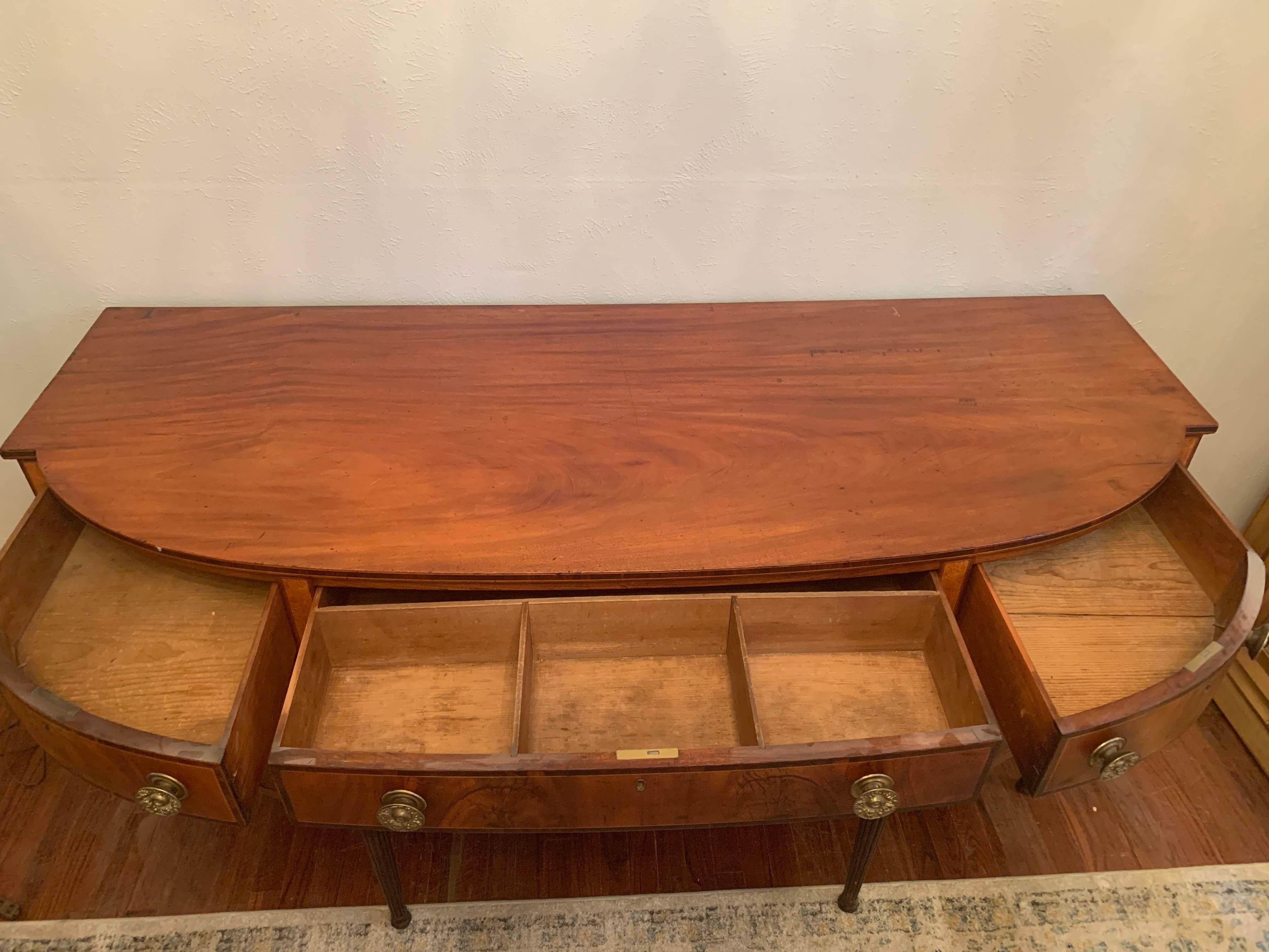 Beautiful American Sheraton/Federal 19th century bow front mahogany sideboard finely constructed with flowing grains of mahogany veneers throughout the front. Features bottle drawers, flanked by convex side drawers on tapered legs. Embellished with