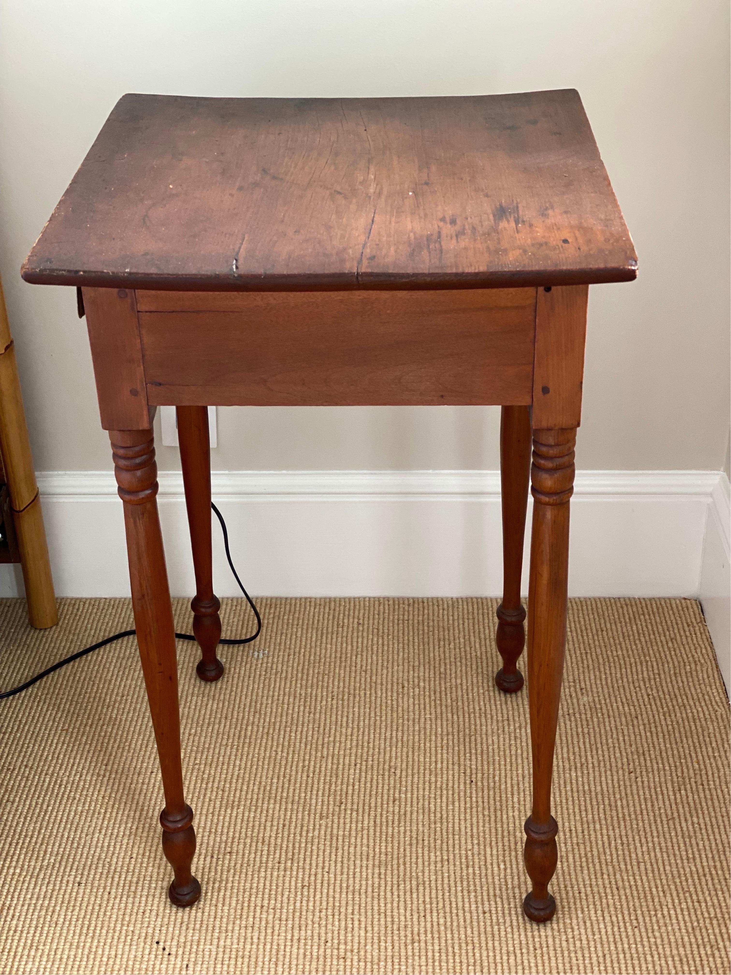 American Sheraton maple single drawer stand, early 19th century.
A single drawer fitted with a pair of decorated brass knobs. The legs are crisply turned with fine ring turnings terminating in a button foot. Peg construction. Top slightly bowed