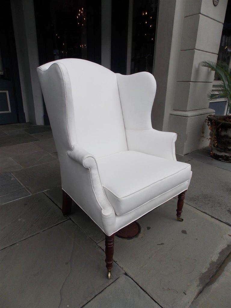 American Sheraton Southern cherry wingback chair with turned bulbous ringed legs, original brass casters, and splayed back legs. Chair is upholstered in white muslin with horse hair and cotton padding. Secondary wood consist of cherry and ash, Early