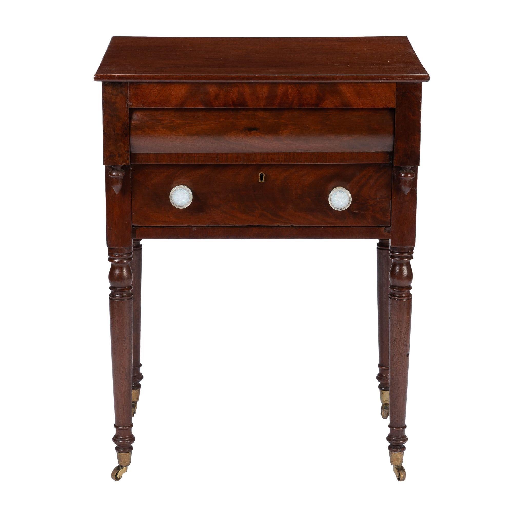 American Sheraton two drawer mahogany and book matched mahogany veneered work table. The projecting blind pillowed top drawer creates a recess for the flat front lower drawer, which is fitted with pressed opaline glass drawer pulls. The projecting
