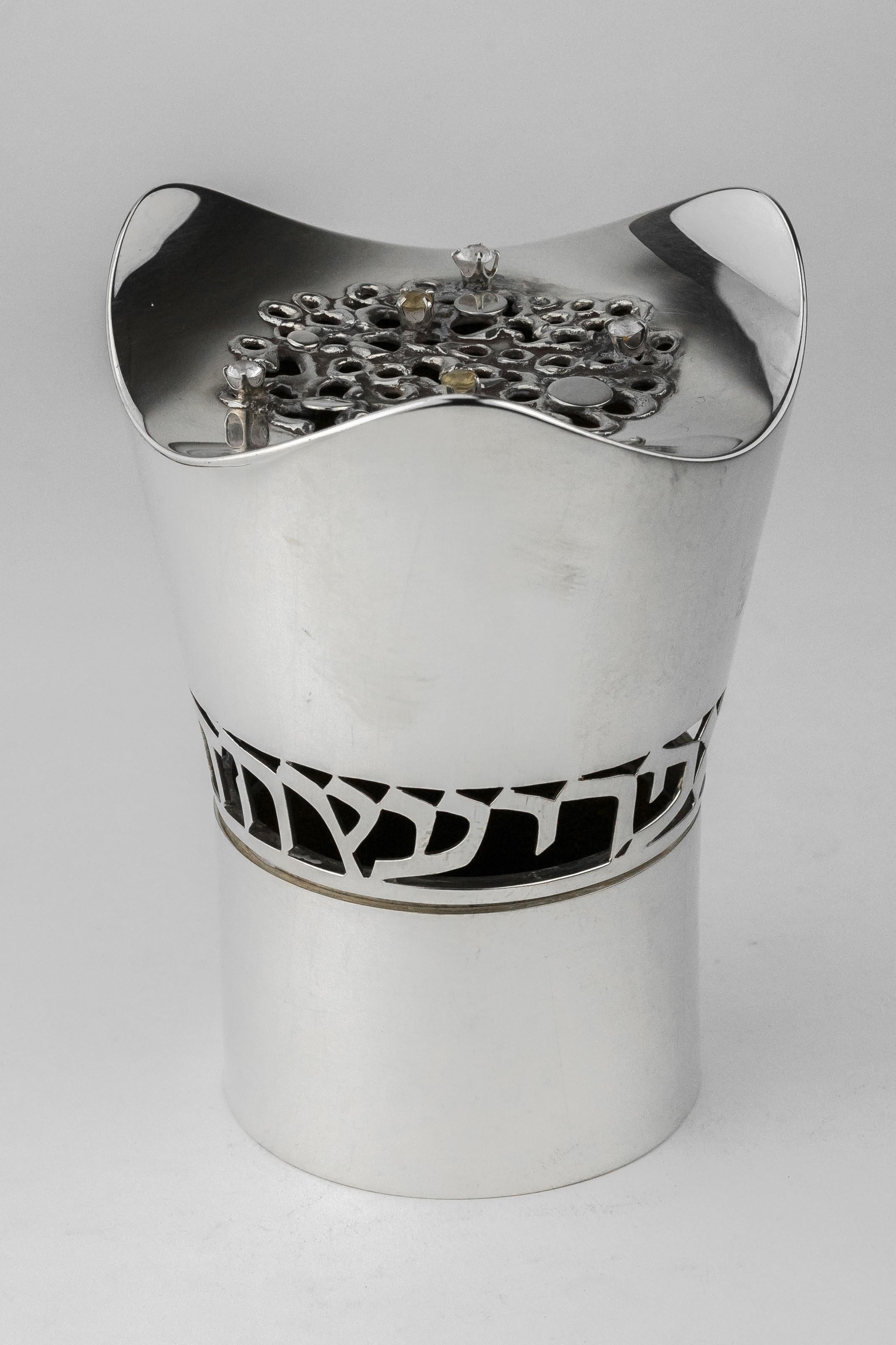 American sterling silver Etrog container, Moshe Zabari, New York, 1970.
Cylindrical shape flaring to three graceful arcs at top surrounding pierced center with semi-precious stones and with pierced Hebrew letters around cylinder which read: 