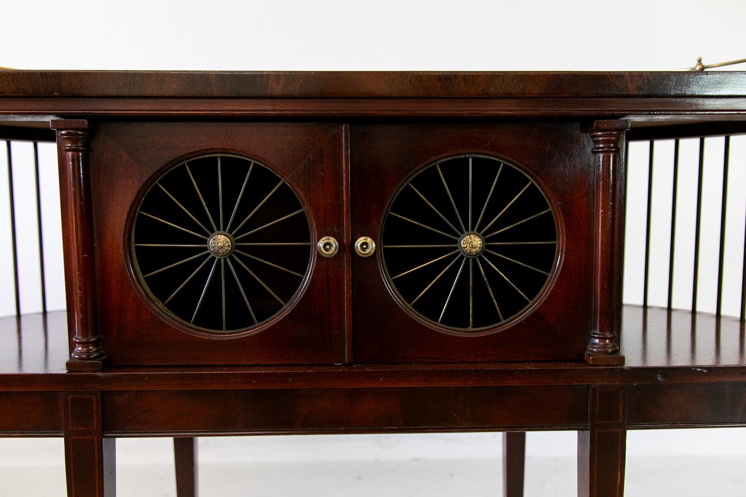 American solid mahogany console table has the original brass gallery and wire wheel doors. The original hardware is polished and lacquered for ease of maintenance. The top has a gold tooled leather center panel crossbanded with crotch mahogany. The