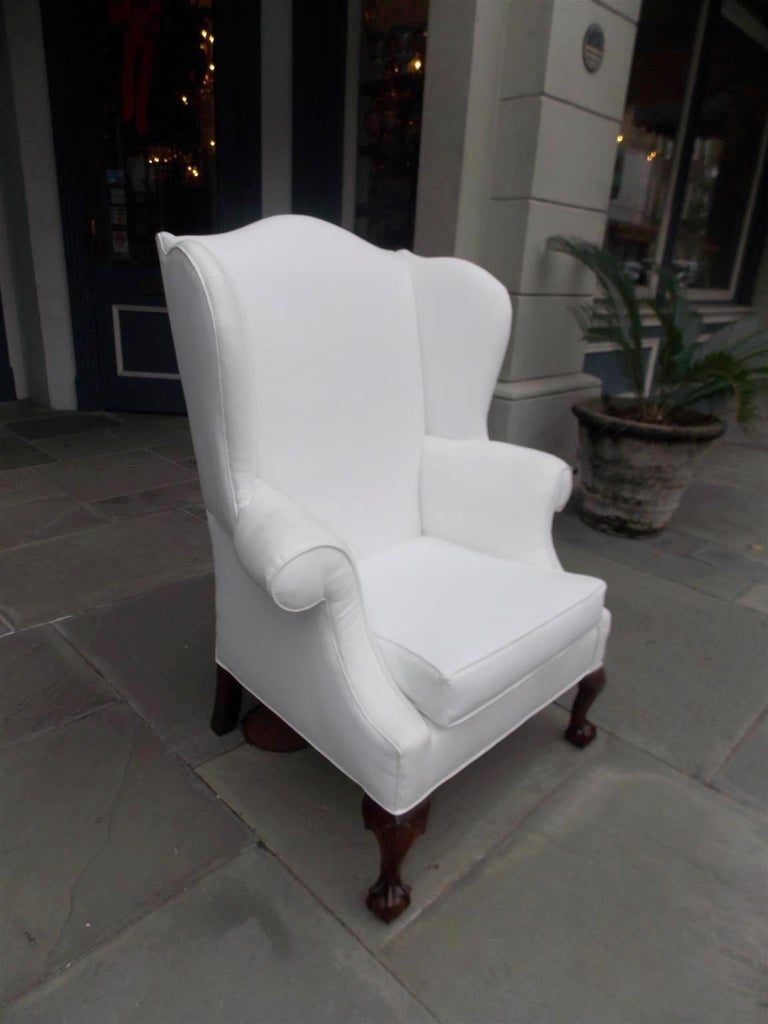 American Southern Chippendale mahogany wing back chair with serpentine back, flared wings, flanking scrolled arms, removable seat cushion, and terminating on claw and ball feet. Secondary wood consist of bald cypress and tulip poplar. Chair is