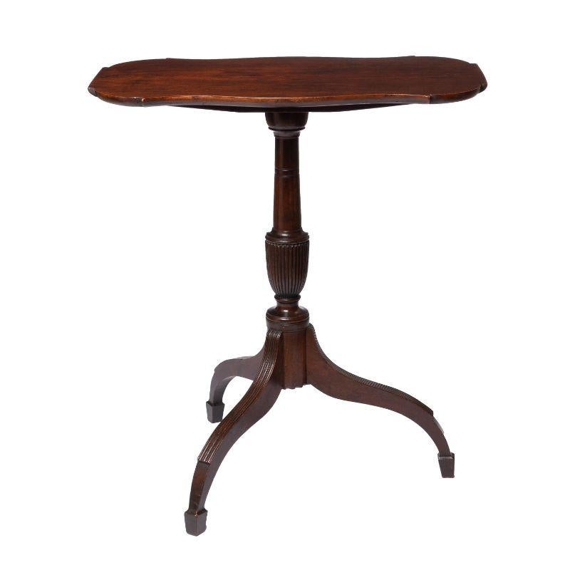 American shaped tilt-top candle stand. The shaped top is hinged to a block on a pedestal centering on a reeded urn form supported by an arched tripod base. The legs have stop reeded leg caps and terminate in spade feet. Mahogany with American cherry