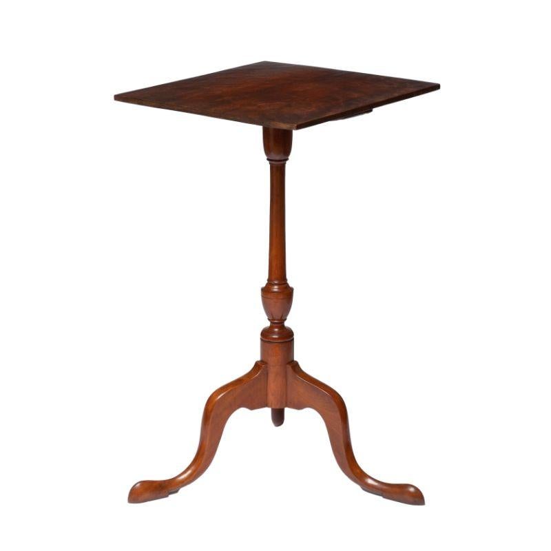 American fixed top candle stand with a square, chamfered edge and figured birch top on a finely turned cherry pedestal with arched tripod cabriole legs. The legs terminate in carved pad pad feet.

American, Portsmouth, New Hampshire, circa 1790.
