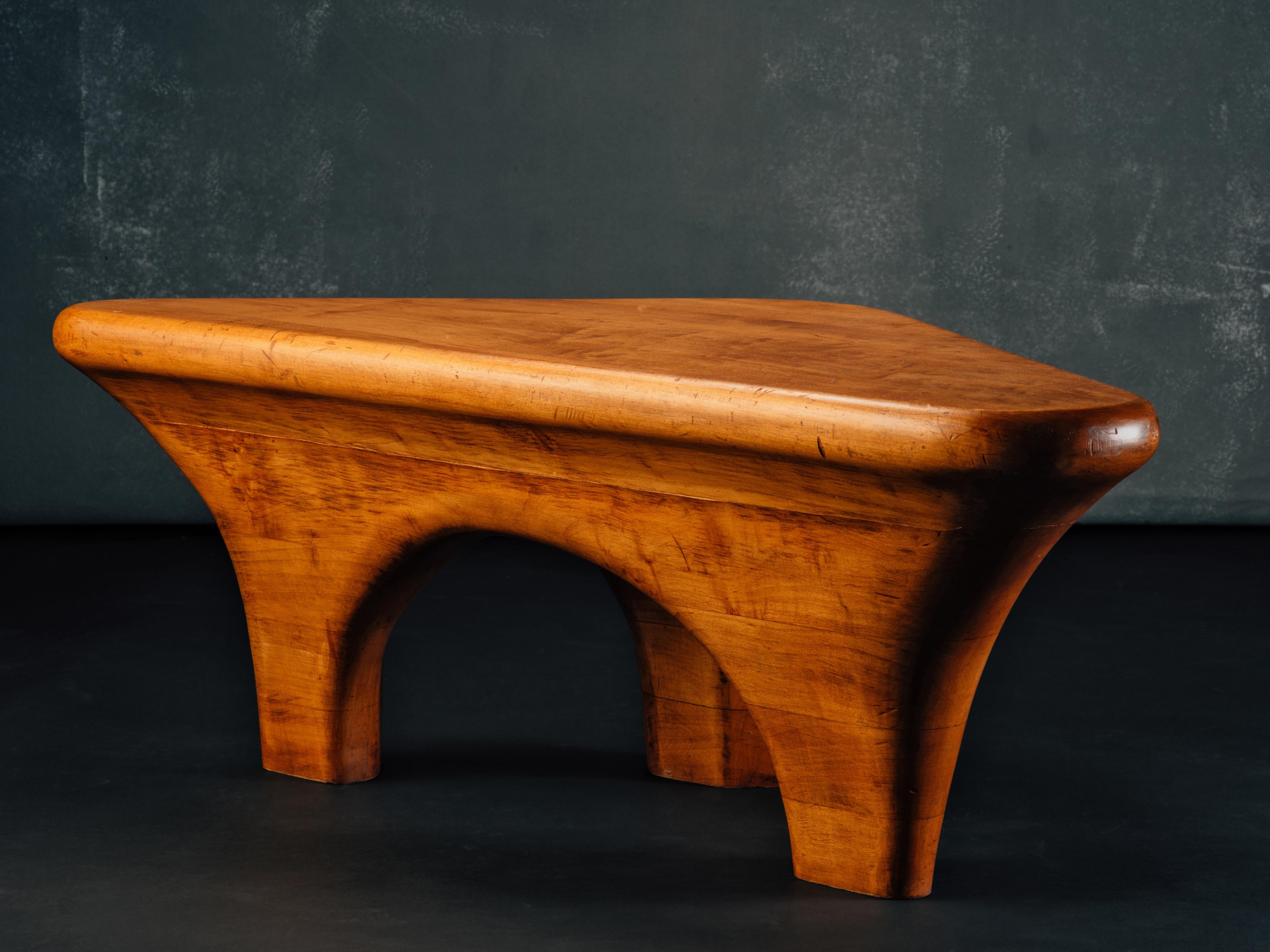 An American Studio table in stack-laminated and sculpted maple, comprising a scalene triangular top with bullnose edge, supported by an architectural, arcaded base. The form is all at once classic, modernist, and tribal, with its original finish
