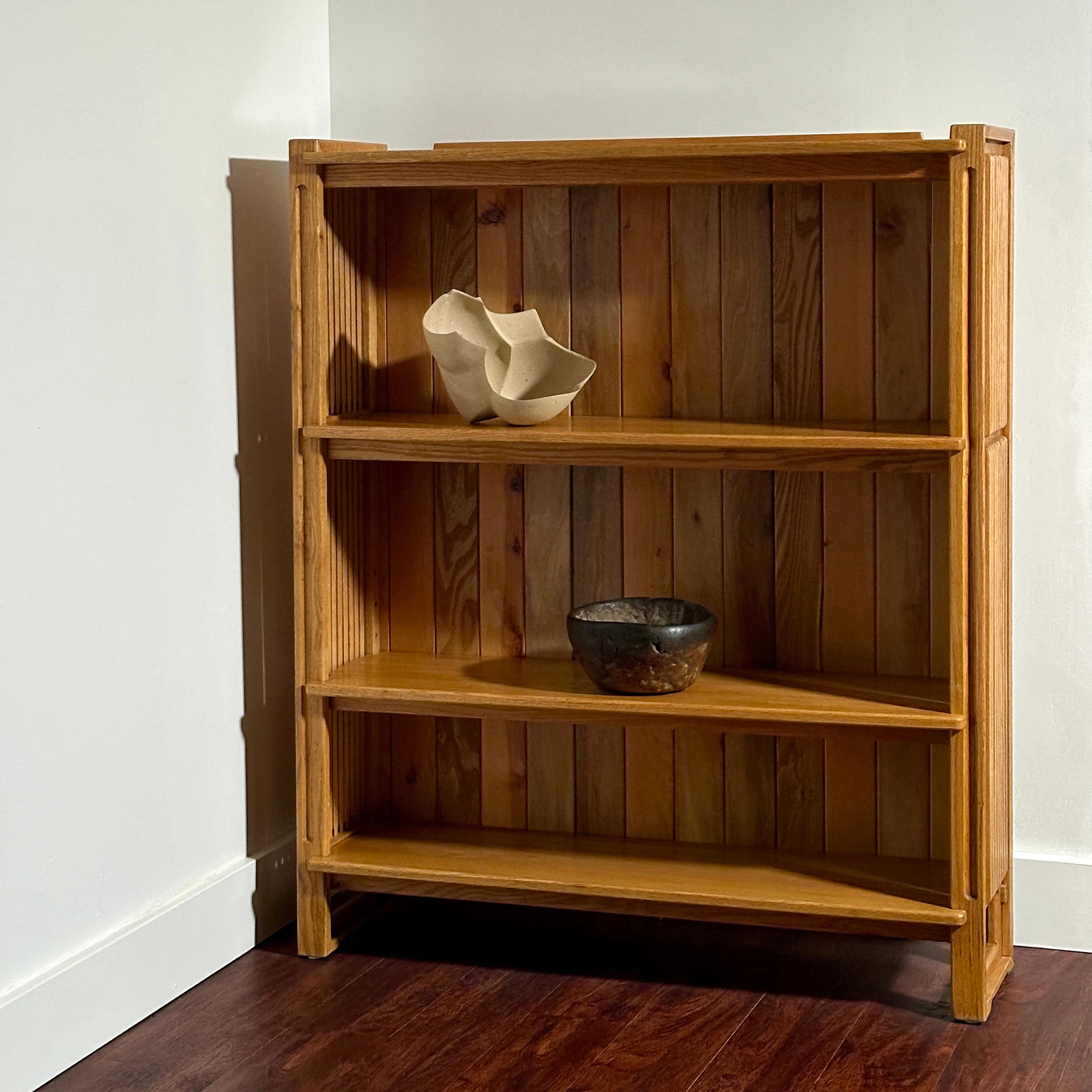 Libreria in rovere massiccio con fianchi e schienale a doghe che fluttuano su una base a slitta, progettata dall'artigiano del Missouri Gene Caples. Diplomato al Kansas City Art Institute e alla Cranbrook Academy of Art (dove ha conseguito il Master