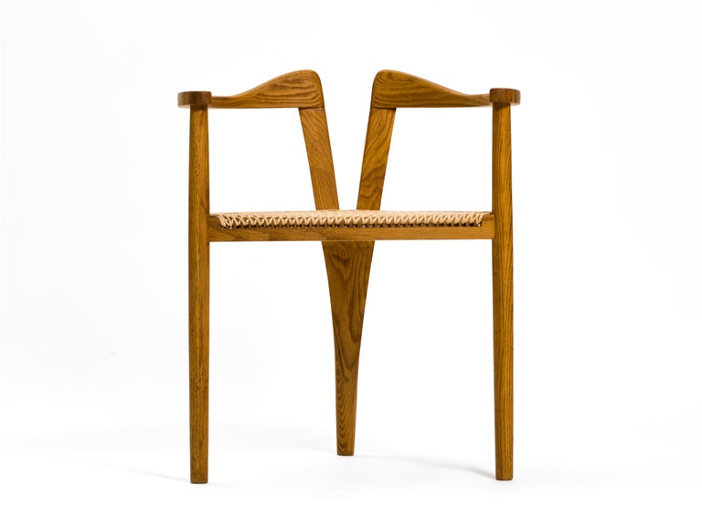 A remarkable, tri-legged studio crafted chair executed in solid oak and finished with a beautifully-patterned handwoven papercord seat. The undulating armrests are supported by Danish-style dowel legs, the one at rear gently arced and then