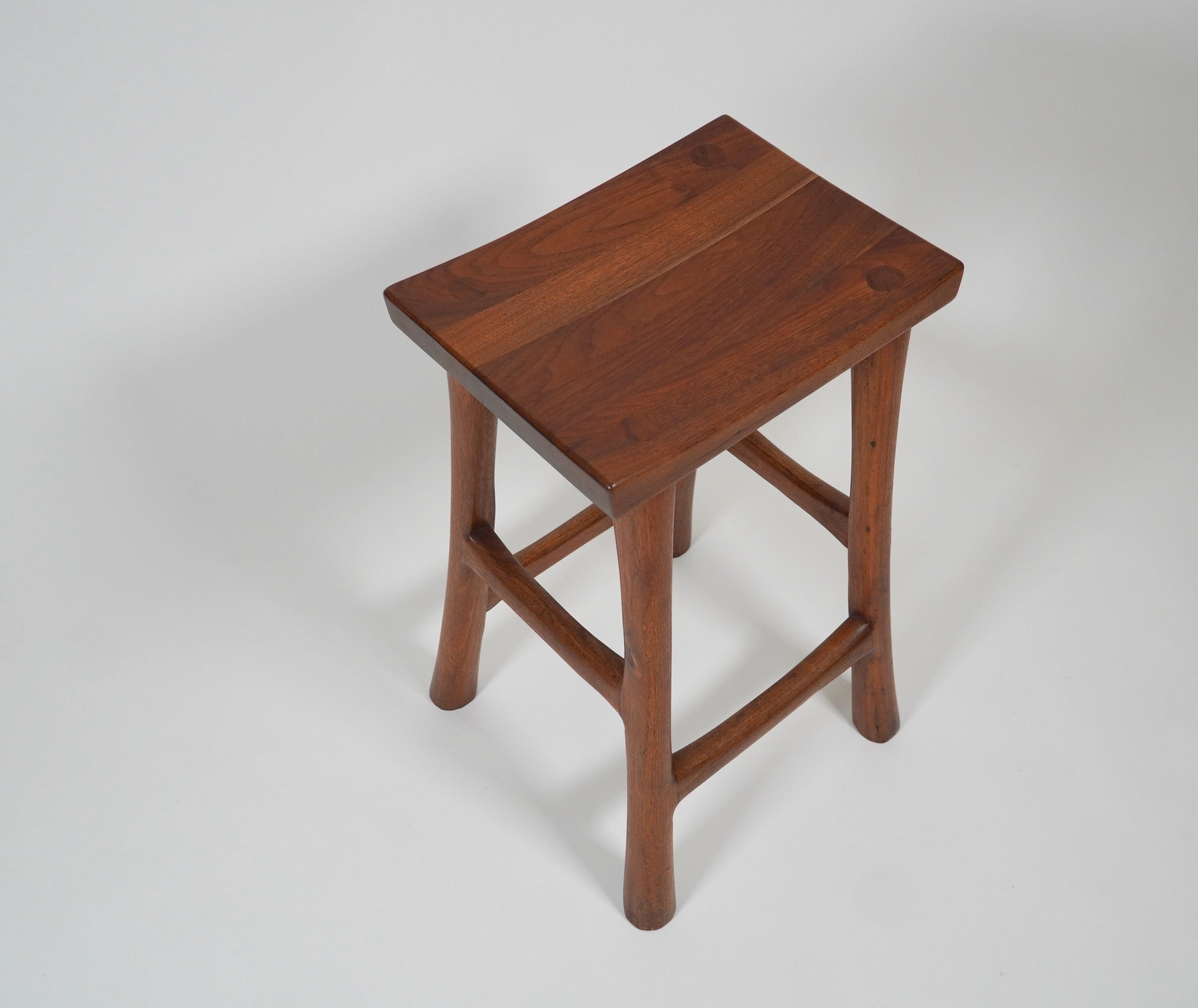 Organic Modern counter height stool by American studio woodworker Wade Andersen, crafted out of walnut with a slight angle pagoda top seat with gracefully tapered legs and cross supports with the leg joints into the seat.