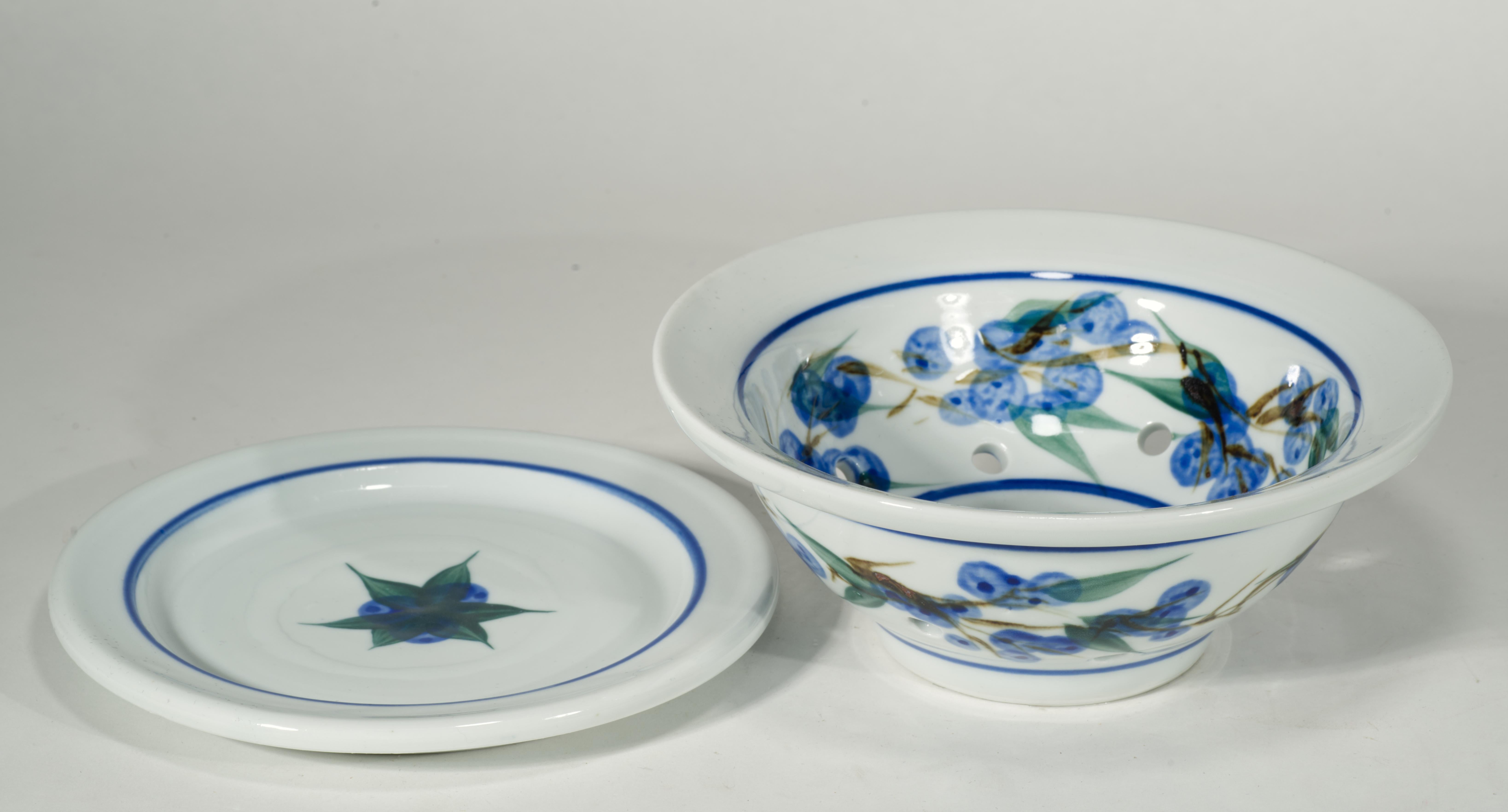 Das charmante Set aus Beerensieb und Unterteller ist mit einem handgemalten Dekor aus Blaubeeren und Blättern versehen. Das Dekor ist sowohl auf der Innen- als auch auf der Außenfläche des Siebs als breites Band angebracht, das durch dünne blaue