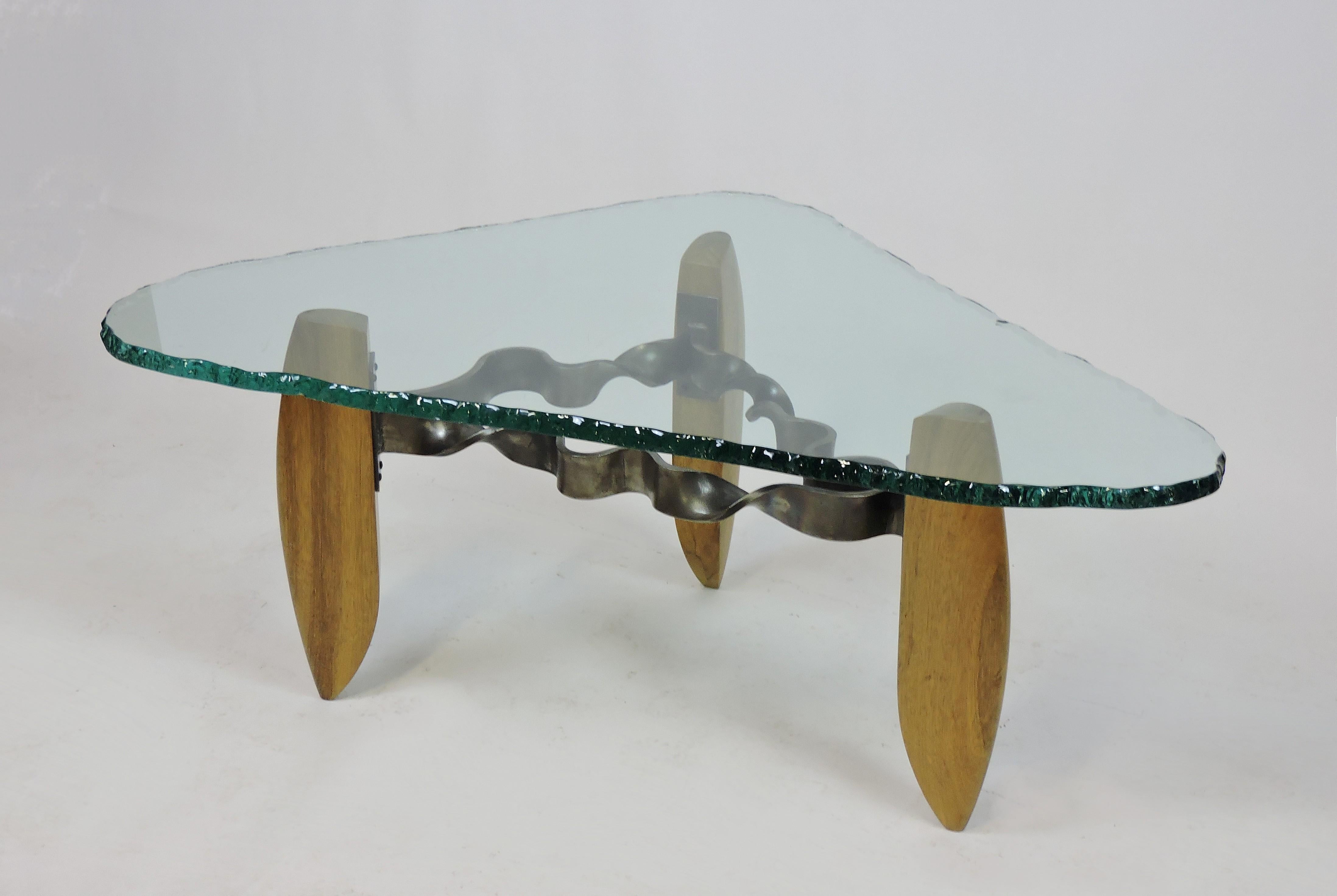 Very cool and unique hand made coffee table in the style of Silas Seandel. This high quality table has thick twisted metal stretchers attached to 3 sculpted wooden legs. The top is 3/4 inch thick glass with a decorative chipped edge. Very well made,