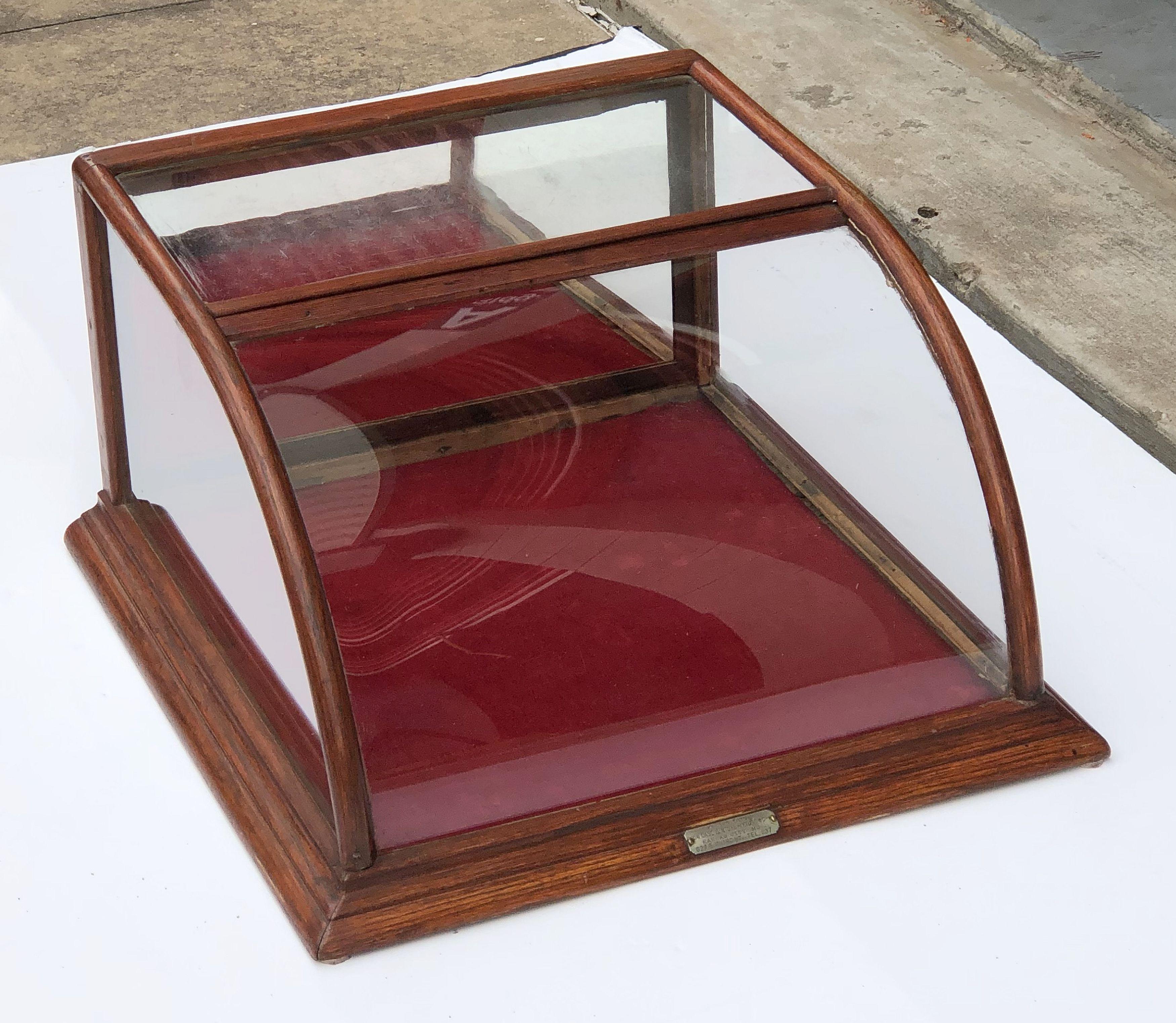 A fine American table top display case or showcase fixture (vitrine) featuring a curved glass front and glass sides, framed in wood, with mirrored interior back that opens to a felt base interior for display.

A great piece of vintage