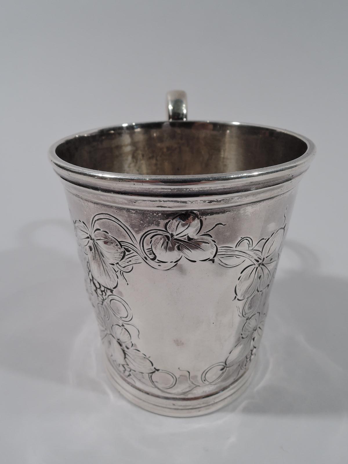 American coin silver baby cup, ca 1850. Gently tapering sides with molded rim and base and high looping s-scroll handle. Ovalish frame (vacant) surrounded by a fruiting berry branch with a profusion of leaves and tendrils. Worn mark. Weight: 4.5