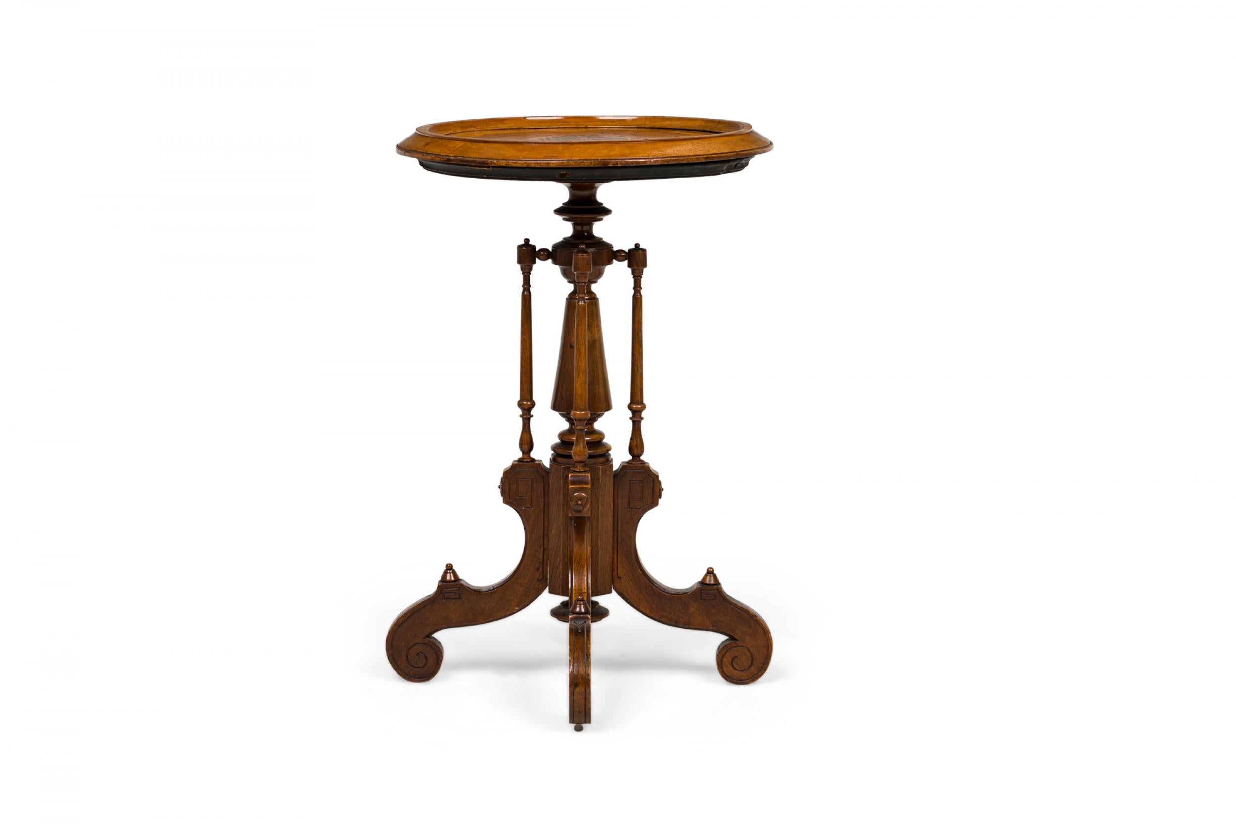 American Victorian wooden plant stand / side table with circular top featuring a central inlaid medallion design, resting on a pedestal base with a central turned post, ending in 4 perpendicular flattened carved legs with scroll feet.