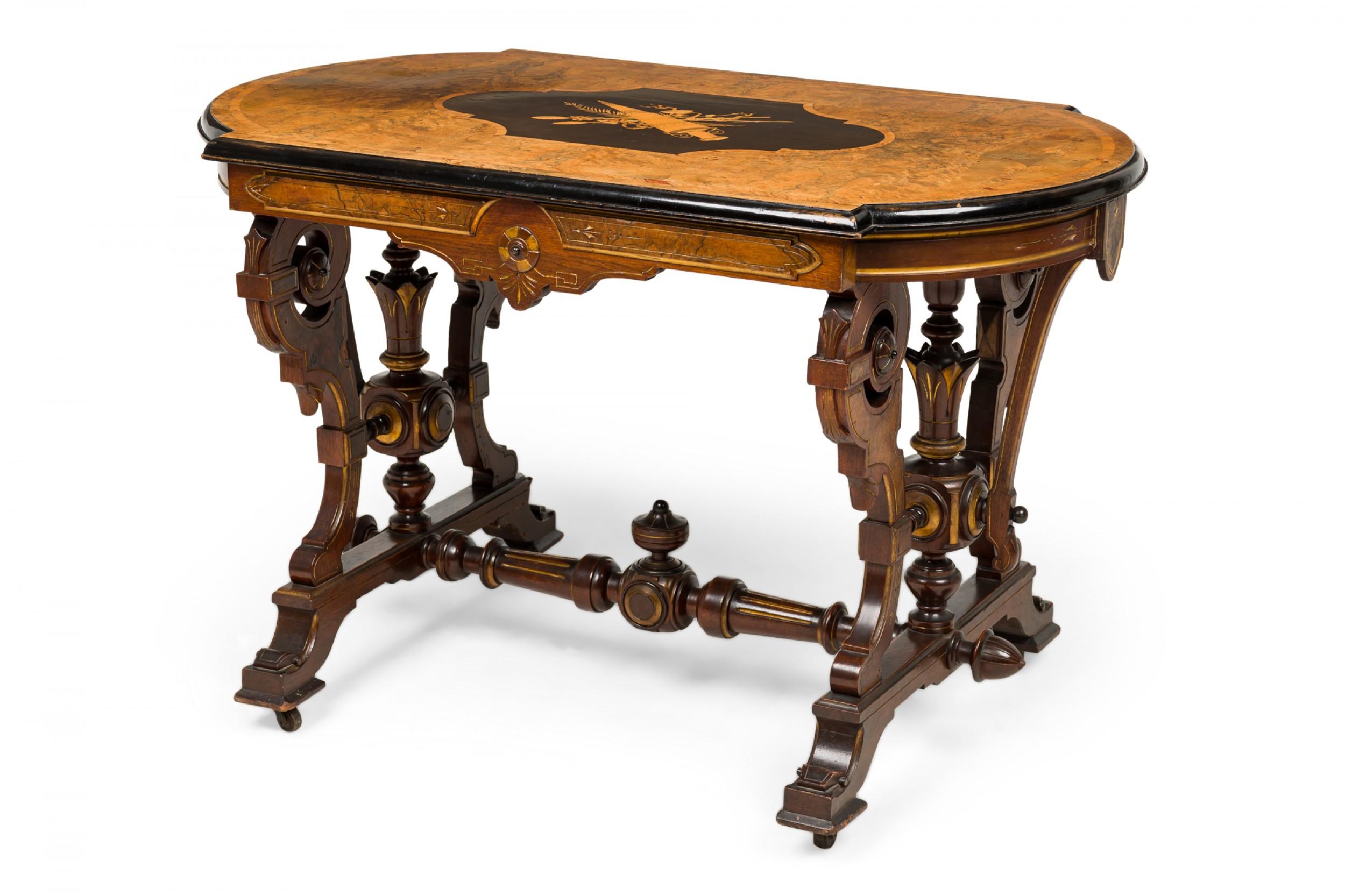 American Victorian mahogany center table with a burl wood top containing an inlaid central cartouche depicting a decorative perfume vessel, gold leaf detailing, elaborate concave scroll legs in a flattened style connected by a turned wood