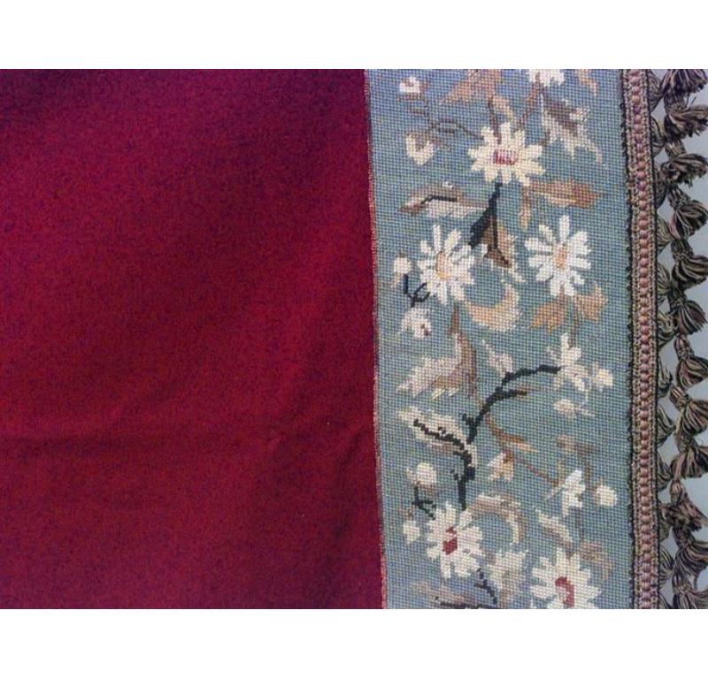 American Victorian table cover with solid maroon velvet field surrounded by blue needlepoint border with daisies design and tassel fringe