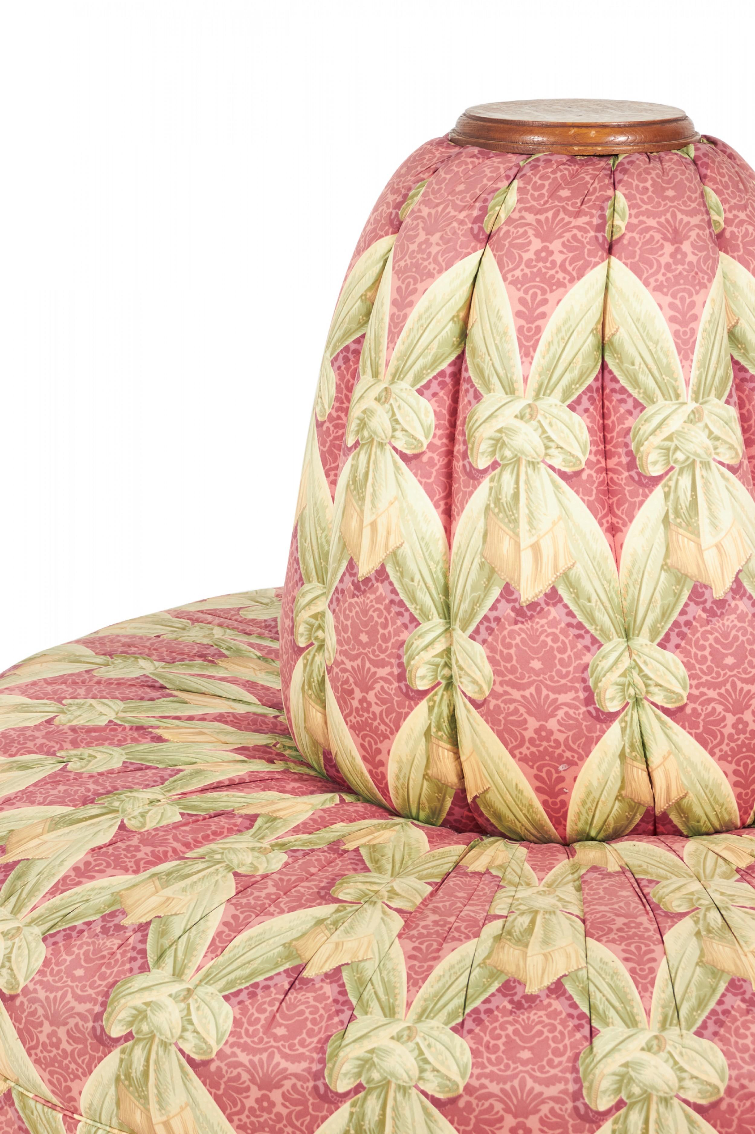 American Victorian circular borne / conversation seat with an oak frame, upholstered in a pink and green bow patterned damask fabric with a channeled center post and pleated seat skirt fabric skirt, resting on oak bun feet.