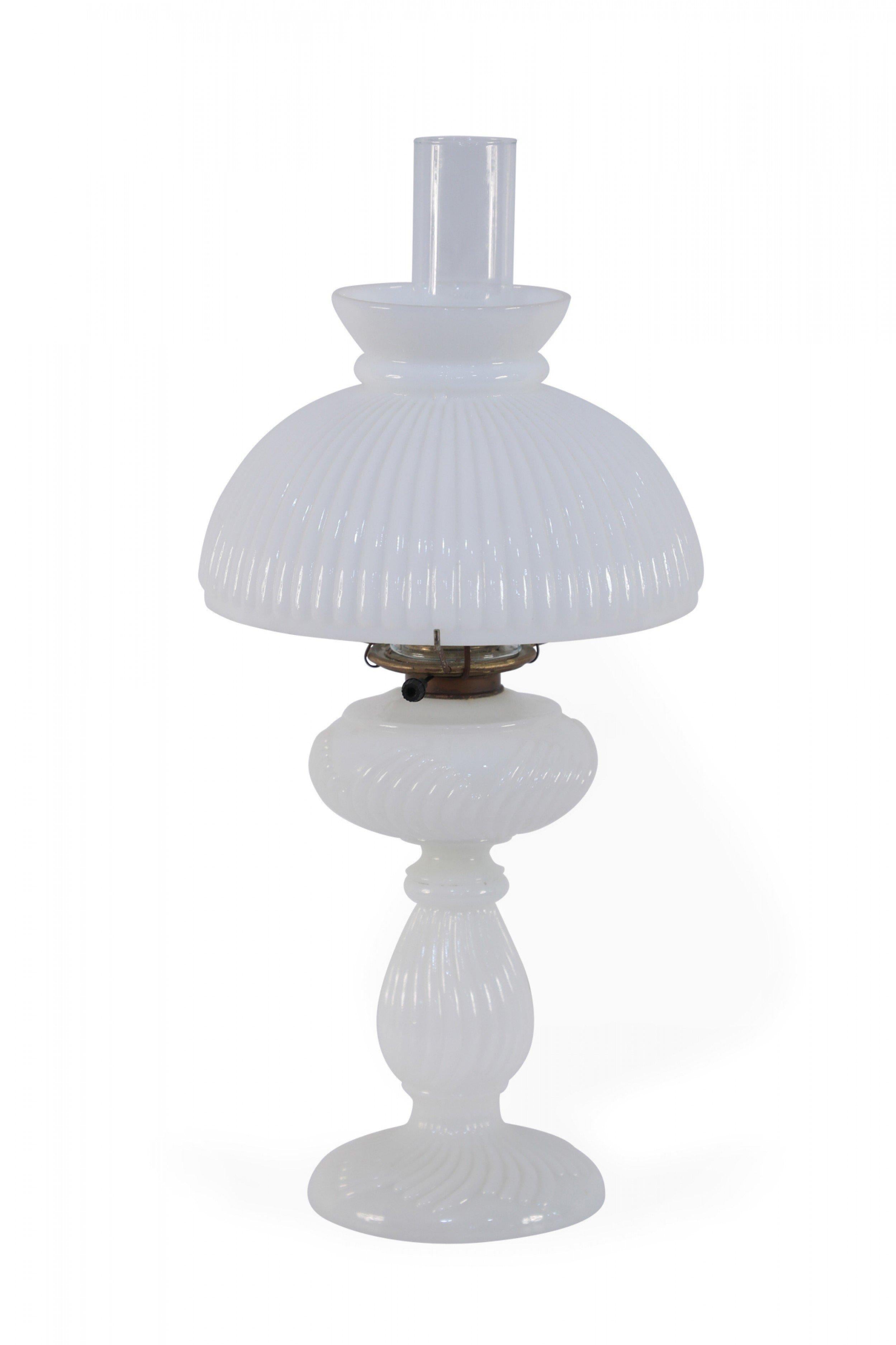 American Victorian ribbed milk glass (oil) table lamp comprised of a shaped glass base with threaded brass hardware and a clear glass hurricane shade beneath a larger ribbed milk glass shade.