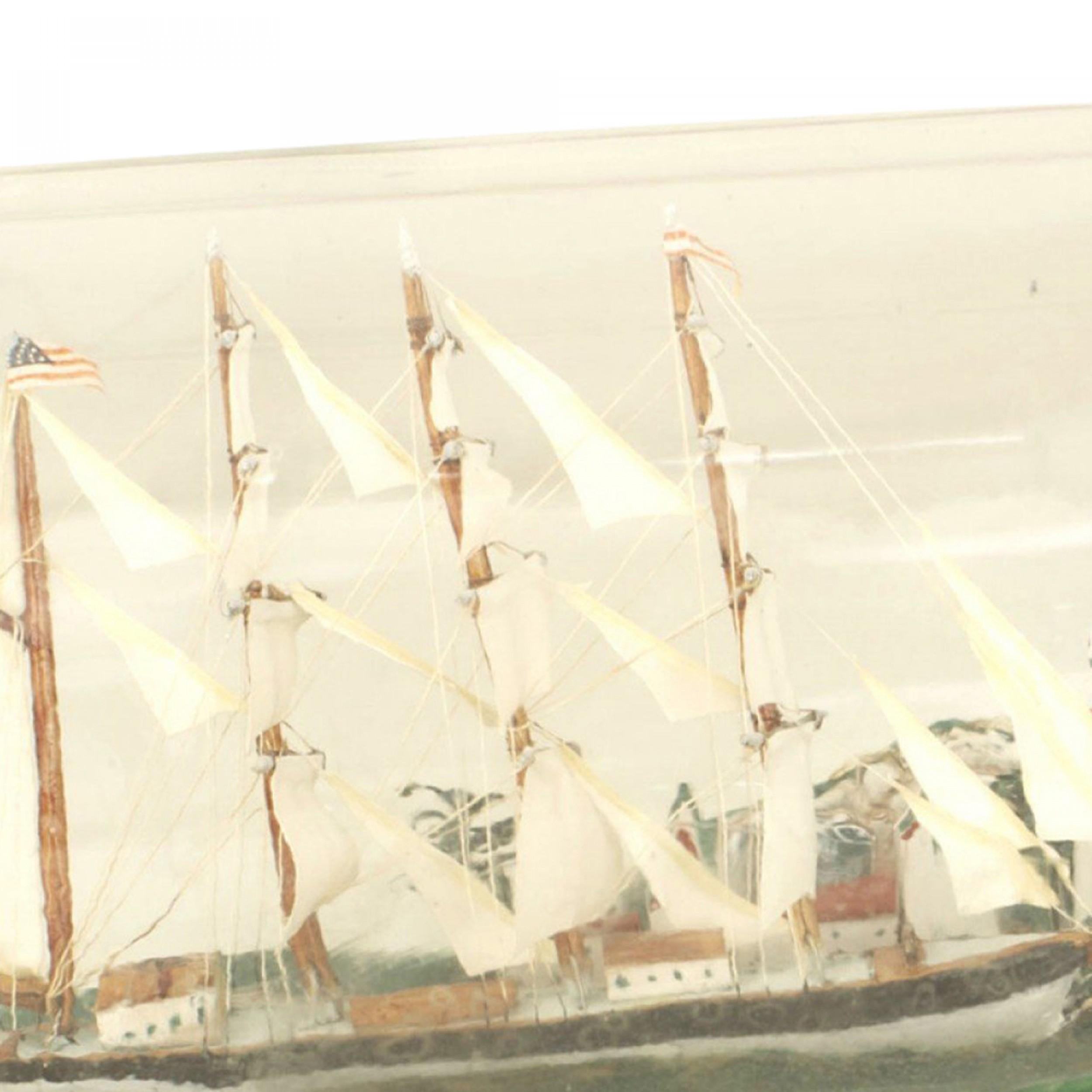 Voilier américain/anglais (19/20e siècle) avec 4 mâts et un phare dans une bouteille en verre de forme bulbeuse sur une base en bois vert.