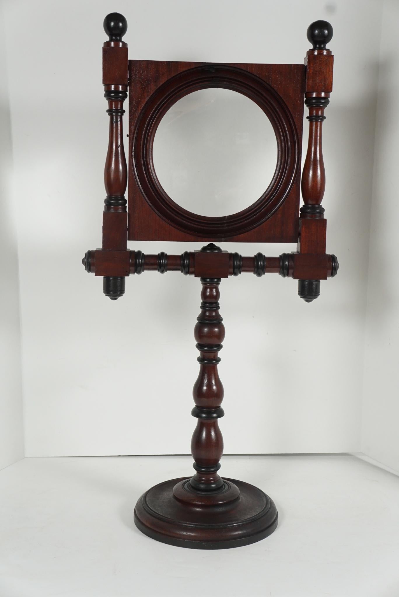 This large American Victorian standing magnifying glass is encased in a carved and turned walnut frame and is adjustable to height with a wooden screw set device. Made circa 1880 the wood is richly colored and has its original finish that has