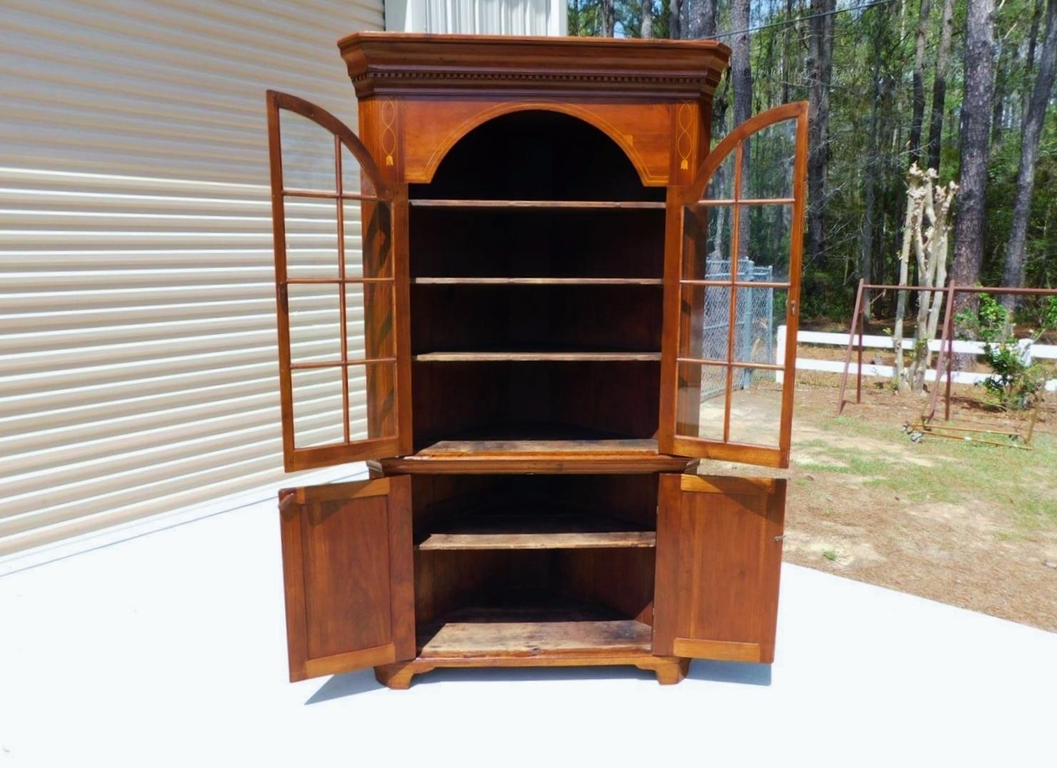 Armoire d'angle en noyer américain incrustée de feuilles de vigne, avec une corniche moulurée, une moulure en denticule sculptée, un corps supérieur flanqué de portes vitrées arquées à charnière en H révélant trois étagères intérieures, un corps
