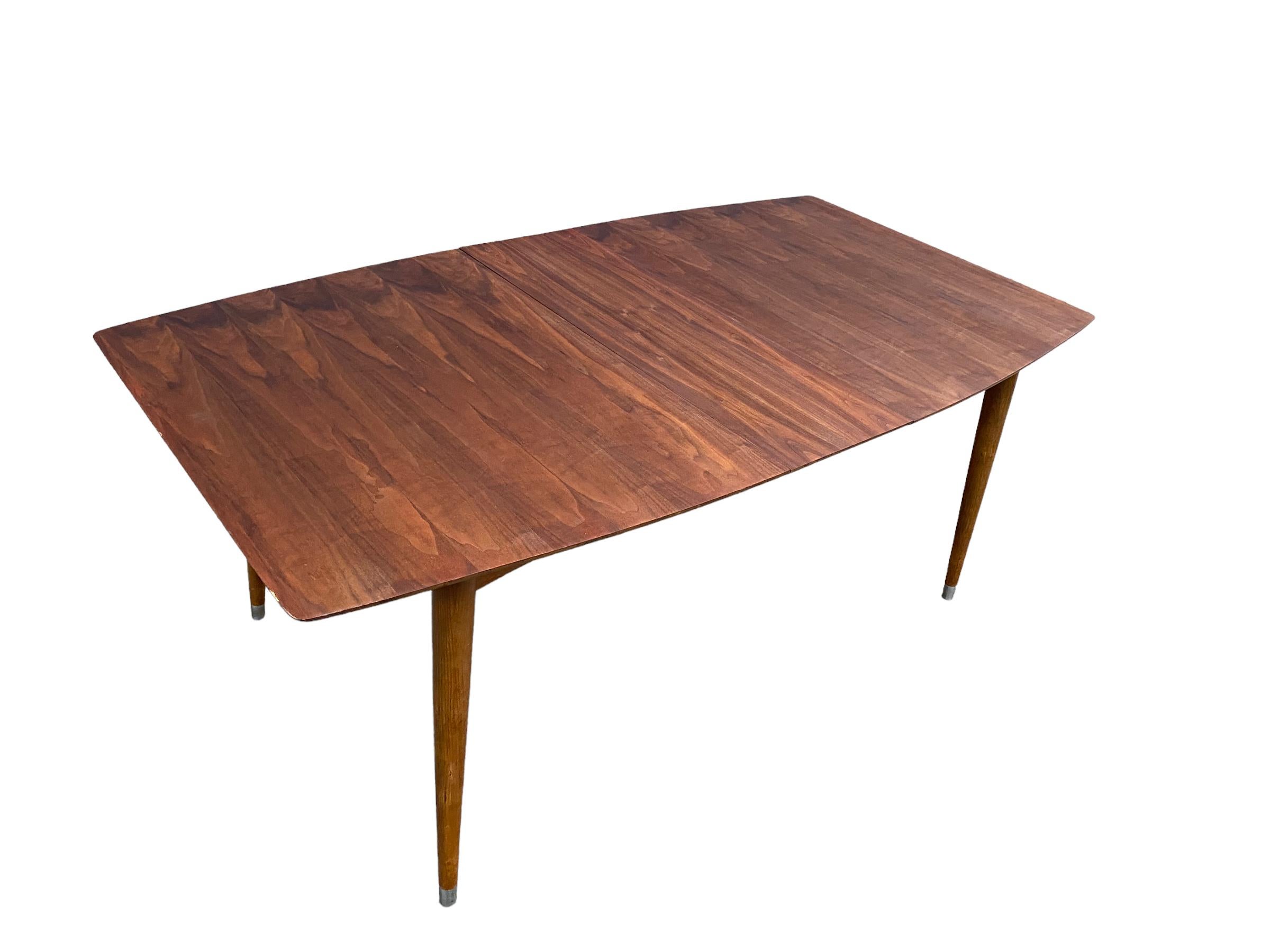 American modern walnut dining table with three leaves. Excellent wood grain on surfboard and tapered legs with metal caps. Made by Mengel Furniture Co. of Louisville, Kentucky. Measures 60” long by 40” wide. Each leaf adds 12” for a maximum length